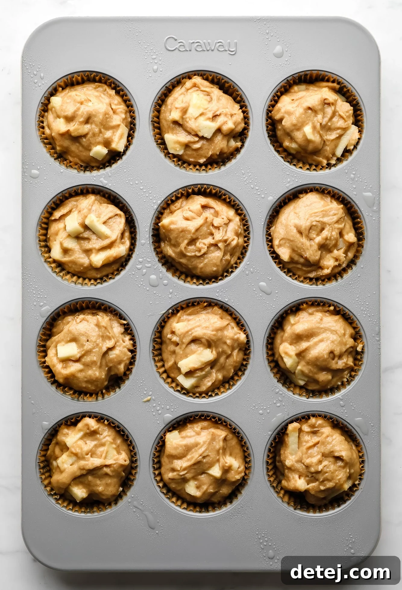 Image of unbaked vegan apple muffin batter in paper liners within a muffin tin.