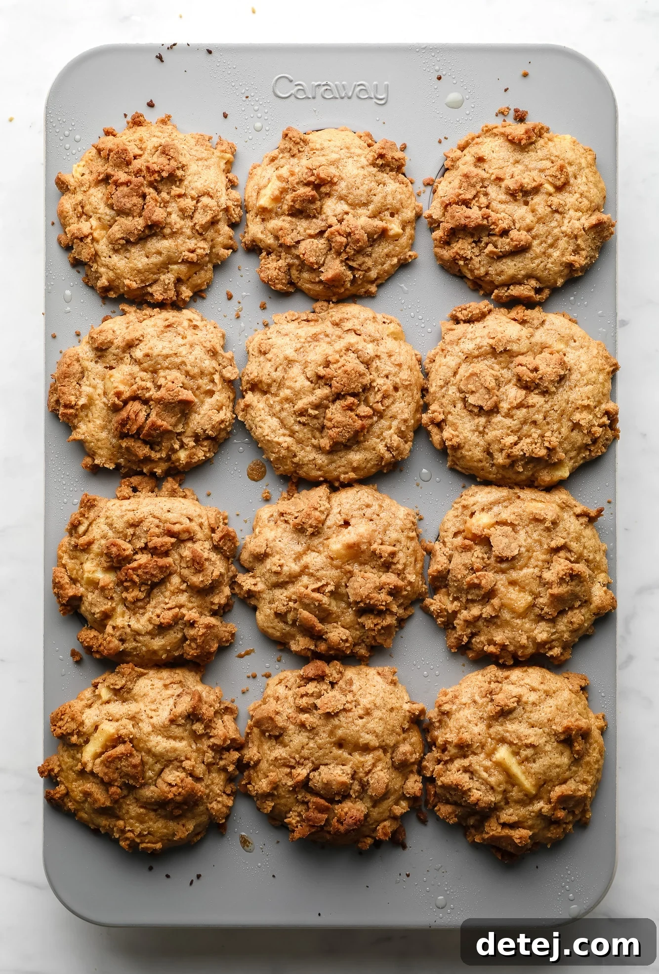 Image of baked vegan apple muffins fresh out of the oven, still in the muffin tin, with golden crumb topping.