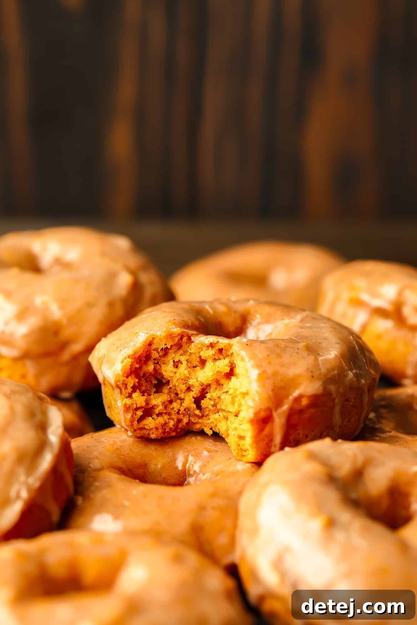 Close up on a fluffy vegan pumpkin donut with a bite taken out of it, revealing its soft interior and the rich cinnamon maple glaze.