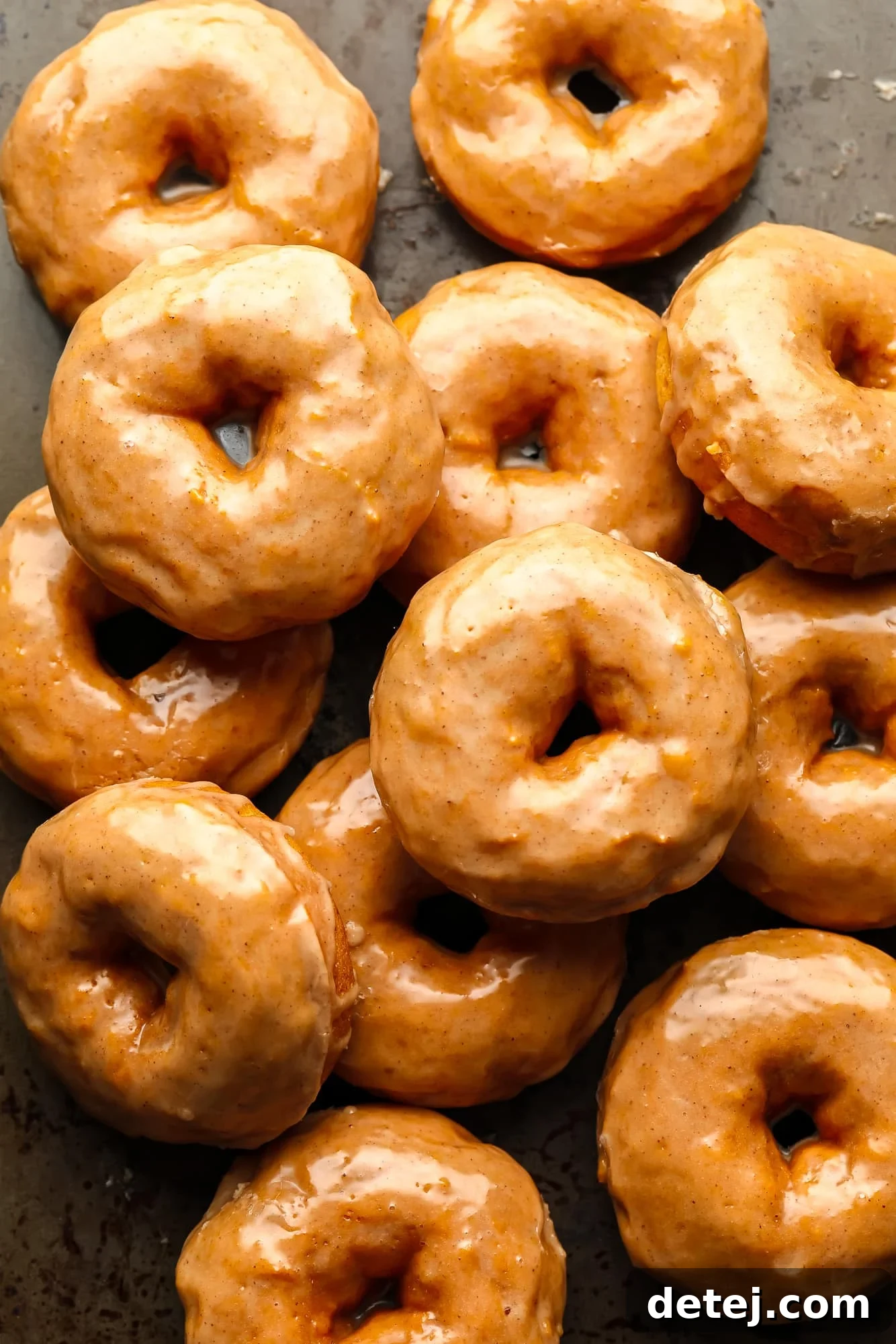 A pile of golden-brown vegan pumpkin donuts generously coated with a glistening cinnamon maple glaze, ready to be enjoyed.