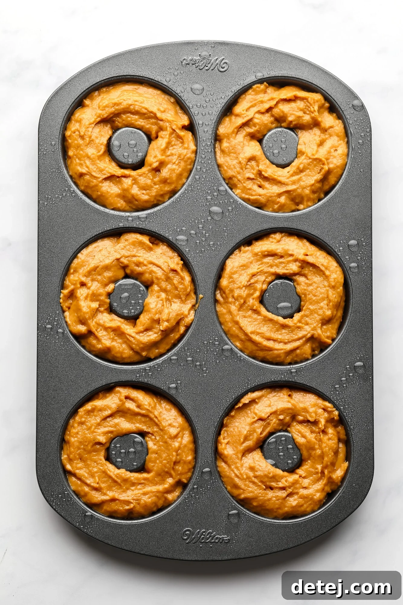 A metal donut pan carefully filled with vegan pumpkin donut batter, ready for baking.