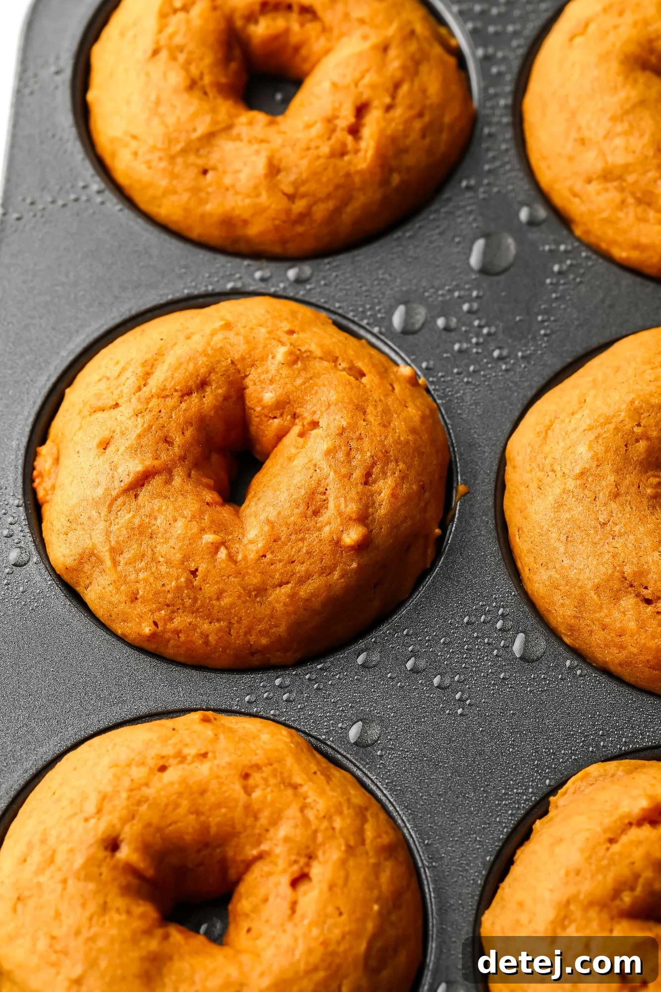 Close up on perfectly formed vegan pumpkin donuts baking in a metal donut pan, their edges slightly browned.