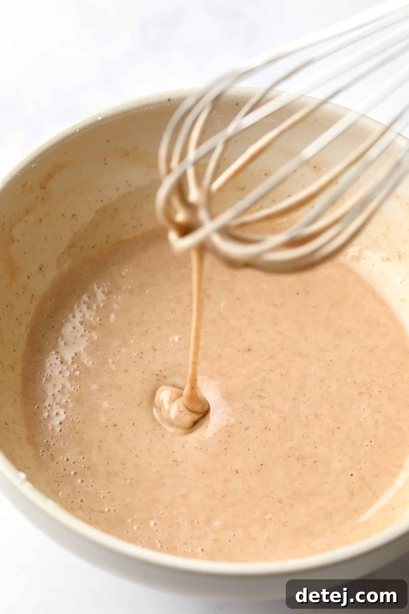 Using a whisk to stir vegan pumpkin donut batter in a mixing bowl, showcasing its smooth, orange texture.