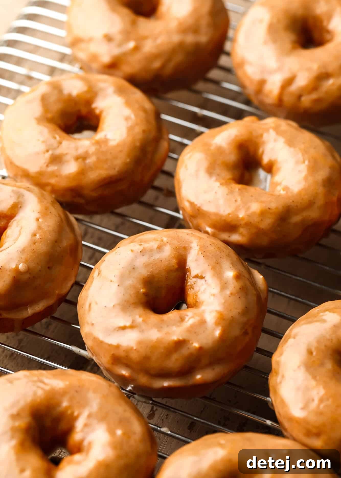 Multiple vegan pumpkin donuts, beautifully coated in a cinnamon maple glaze, arranged on a wire cooling rack.