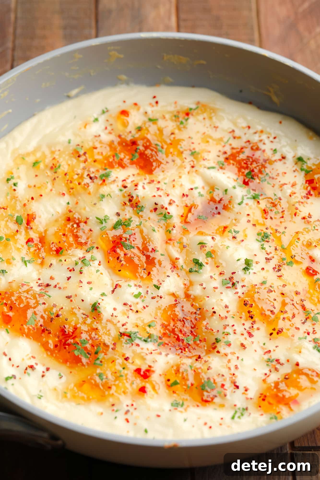 A baked vegan brie dip, rich and creamy, generously topped with a shimmering layer of sweet and spicy pepper jelly, served in a rustic grey saucepan.