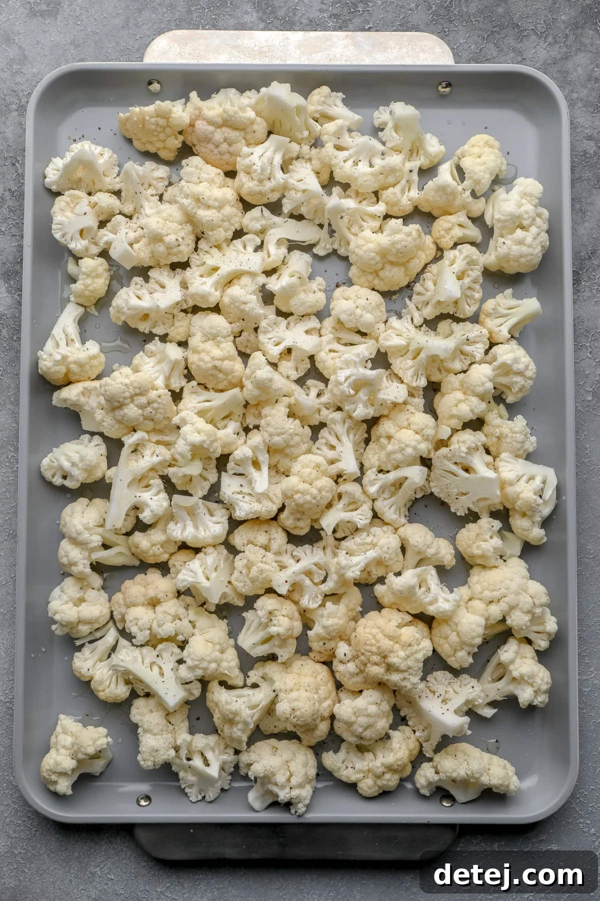 Raw cauliflower florets are neatly arranged on a metal baking sheet, ready for roasting.
