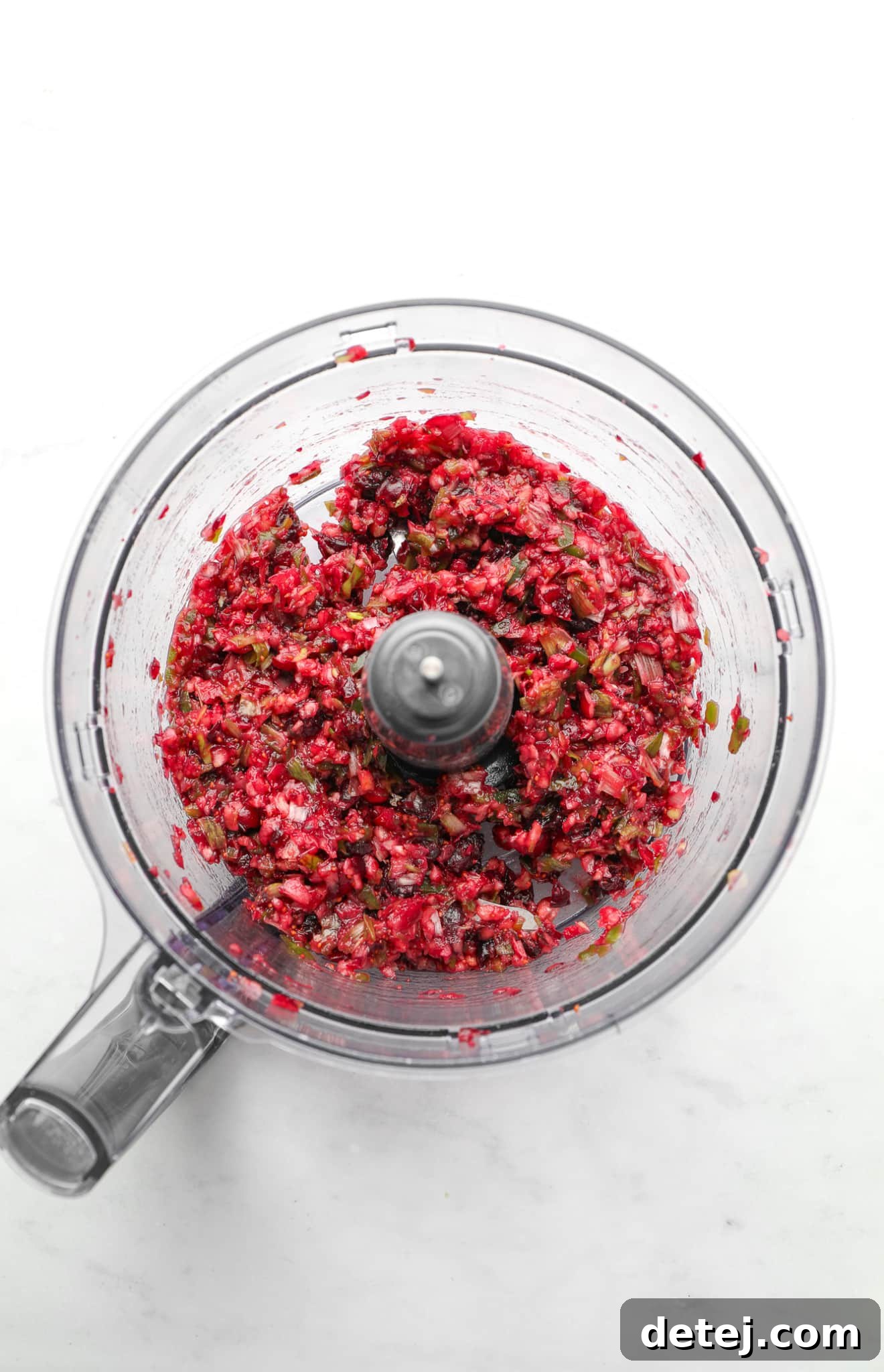 The contents of a food processor after pulsing: a finely chopped, vibrant mixture of fresh and dried cranberries, green onions, and jalapeno, showing a beautiful speckled texture and ready to be incorporated into the dip base.