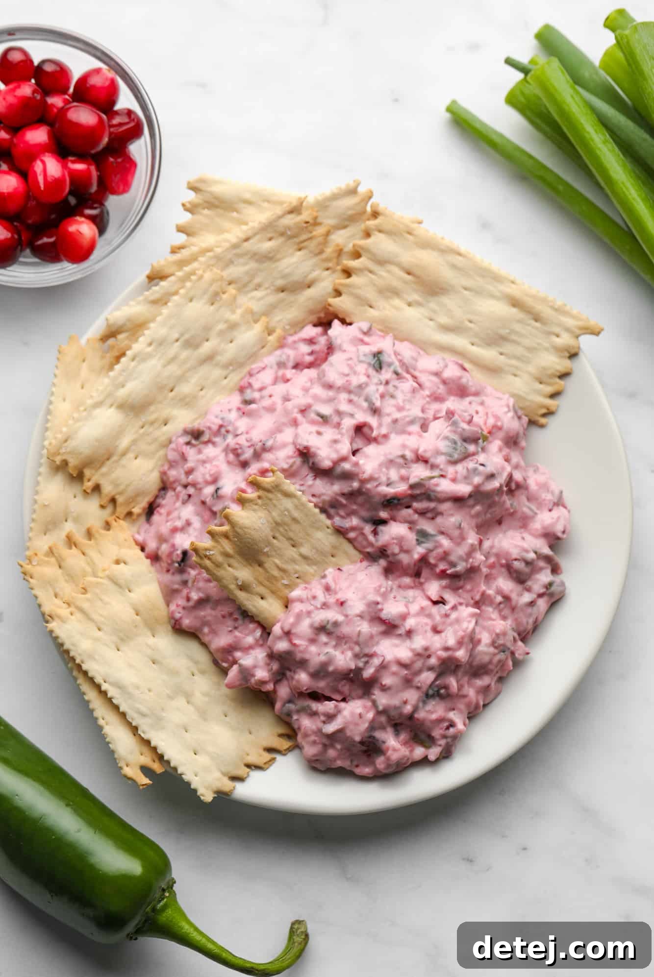 A festive holiday spread featuring the gorgeous pink Cranberry Jalapeno Dip presented in a white serving dish, surrounded by a variety of golden crackers, ready for guests to enjoy at a festive gathering.