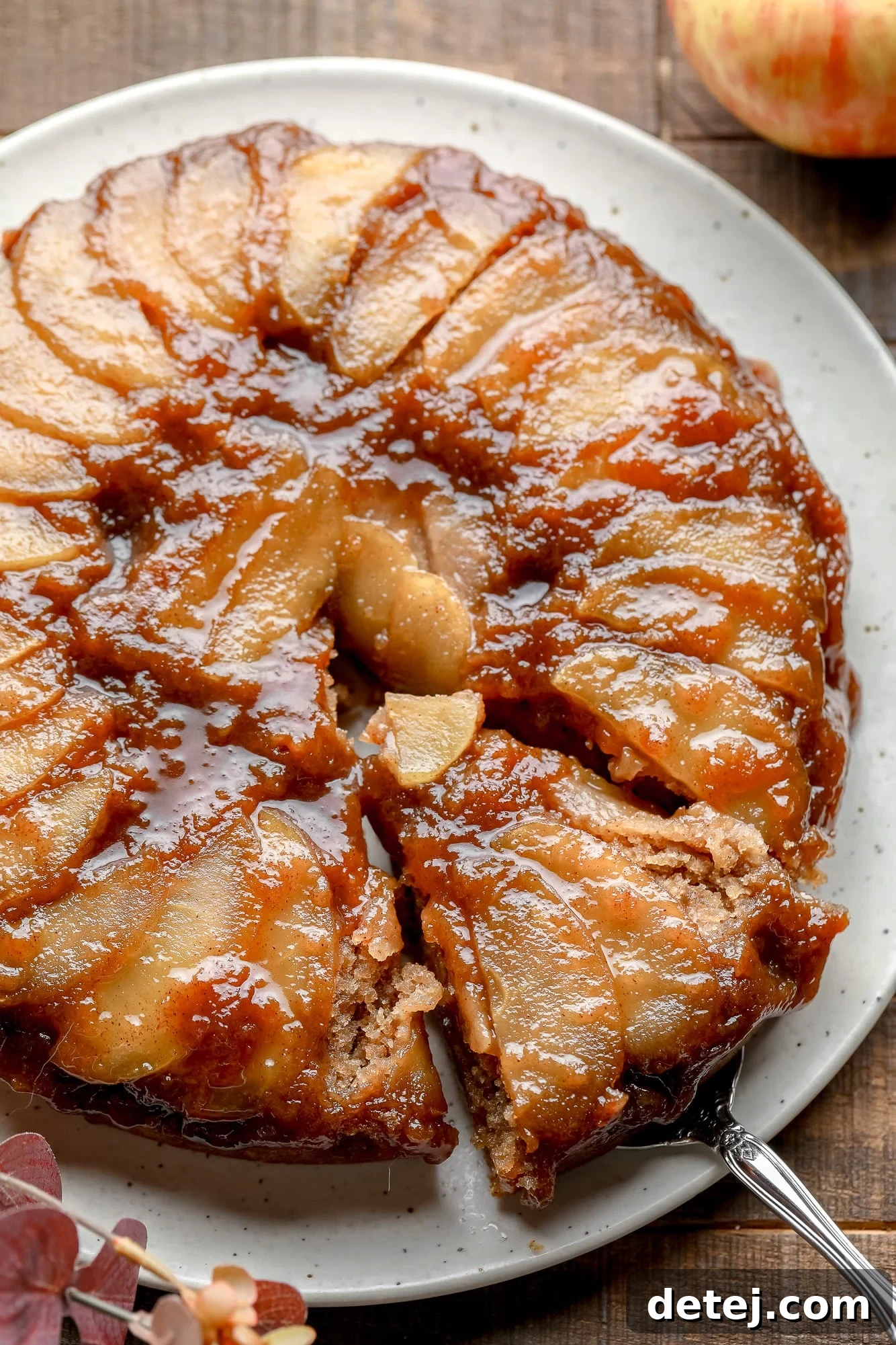 A slice being lifted from an Apple Upside Down Cake on a white plate, showcasing the caramelized apple topping and moist cake beneath.
