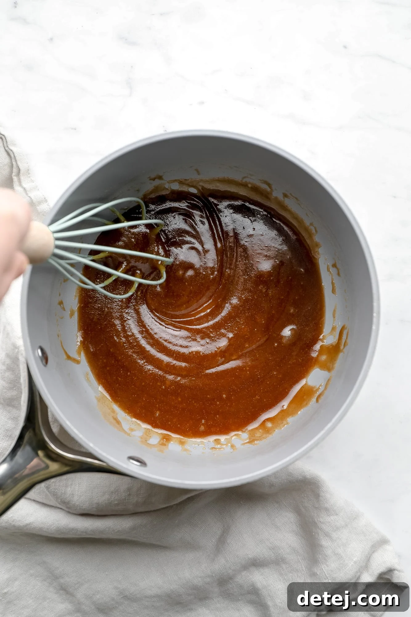 Whisking homemade vegan caramel sauce in a grey saucepan, showcasing the smooth, golden texture.