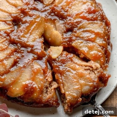Close up on a slice being lifted from an Apple Upside Down Cake on a white plate, showing the caramelized apple topping.