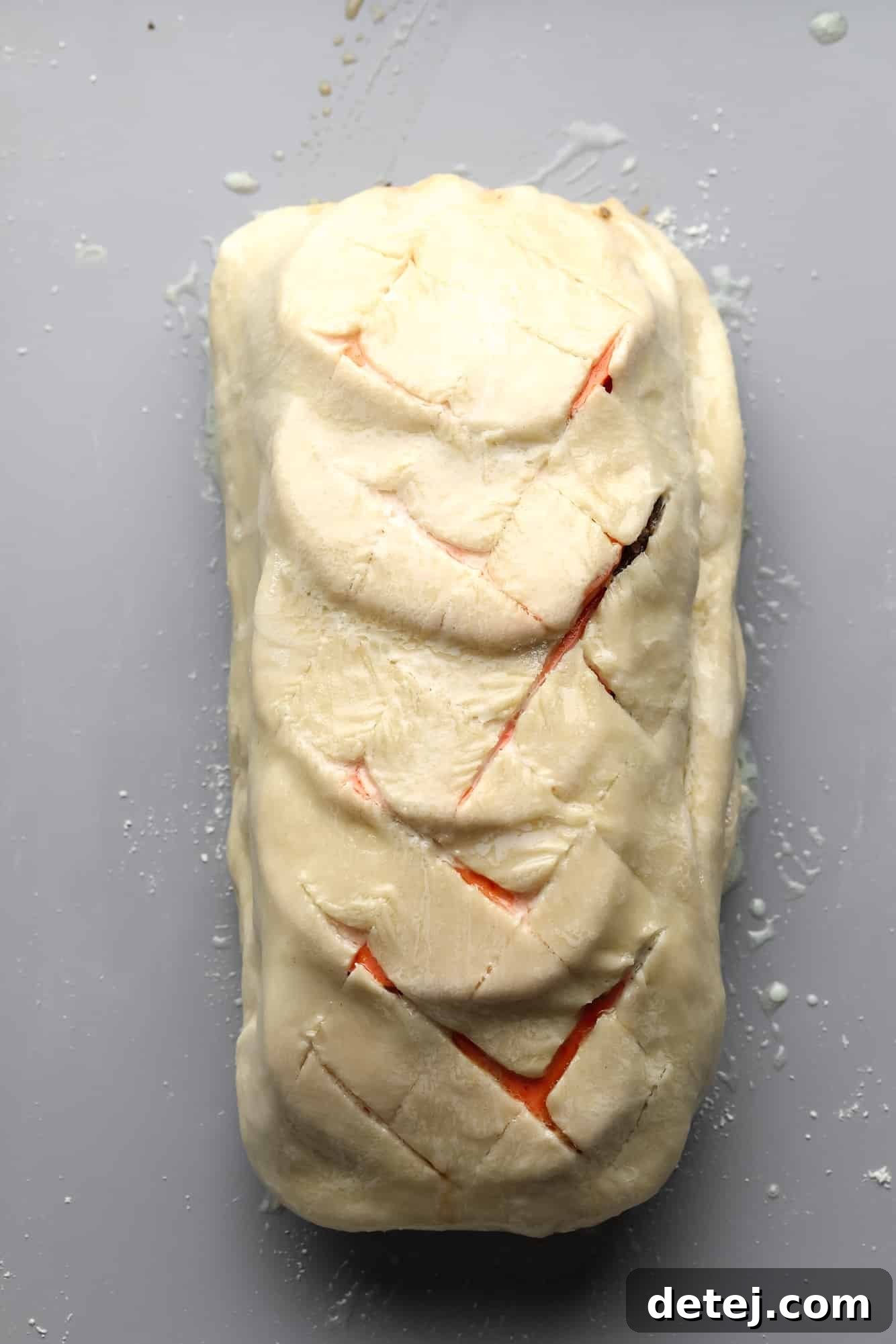 a scored unbaked mushroom wellington on a grey sheet pan.