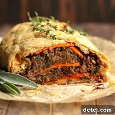 close up on a baked and sliced mushroom wellington topped with fresh thyme.