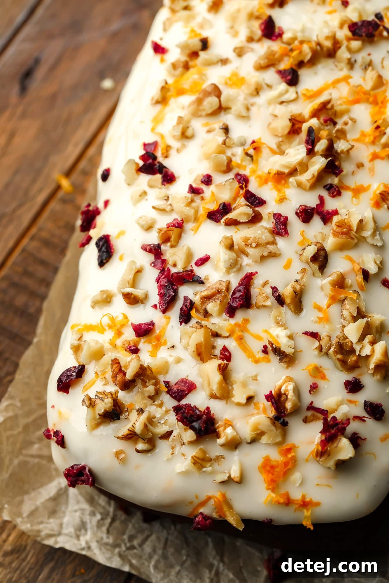 Cozy Gingerbread Bake 12 close up on cream cheese icing decorated with nuts, dried cranberries, and orange zest on a gingerbread loaf.