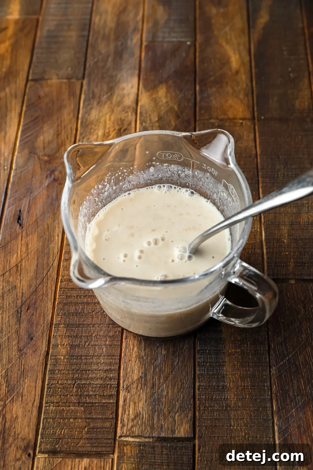 Cozy Gingerbread Bake 4 using a metal spoon to stir a milk and flaxseed mixture in a glass measuring cup.