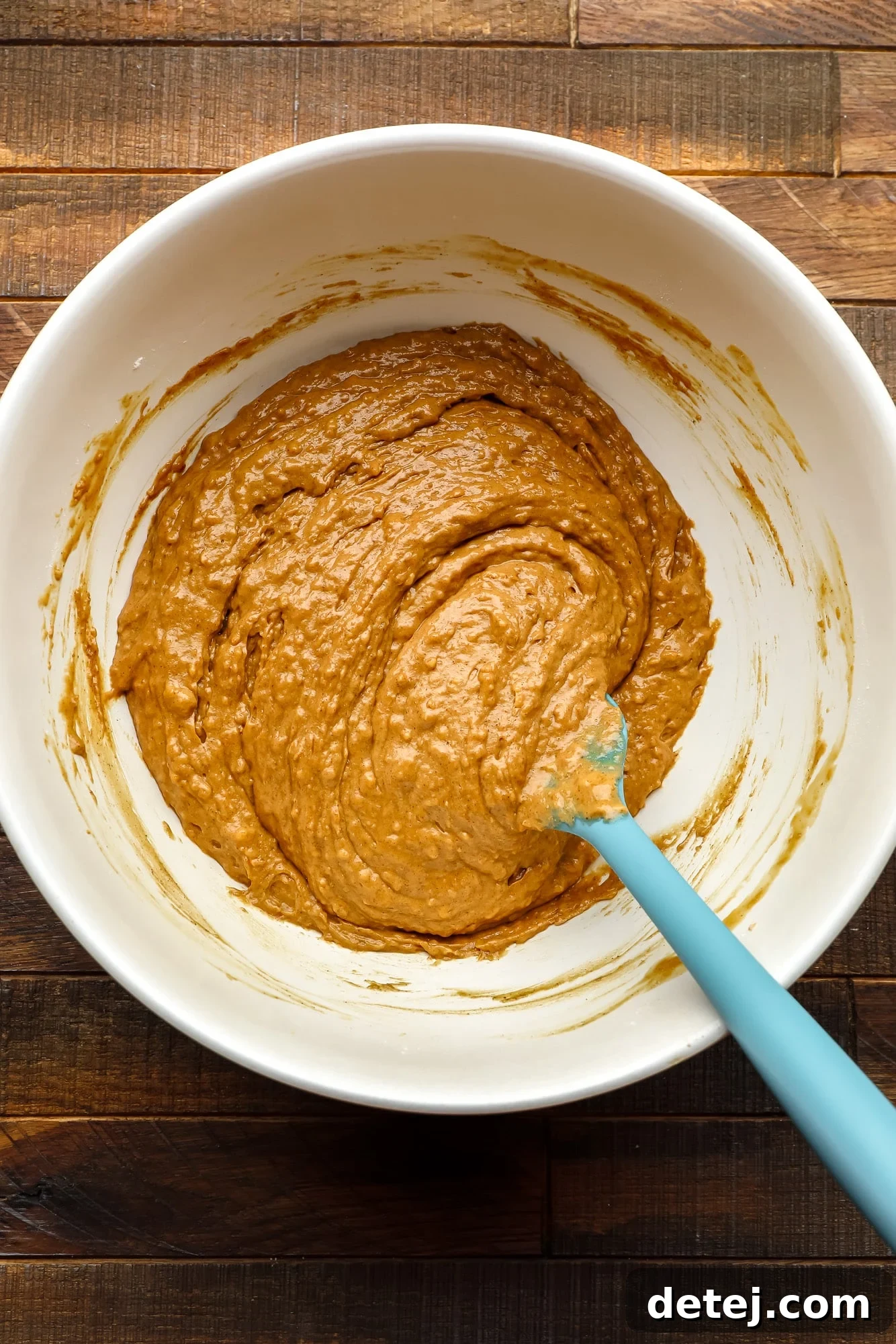 Cozy Gingerbread Bake 7 using a spatula to stir batter for a gingerbread loaf in a large white bowl.