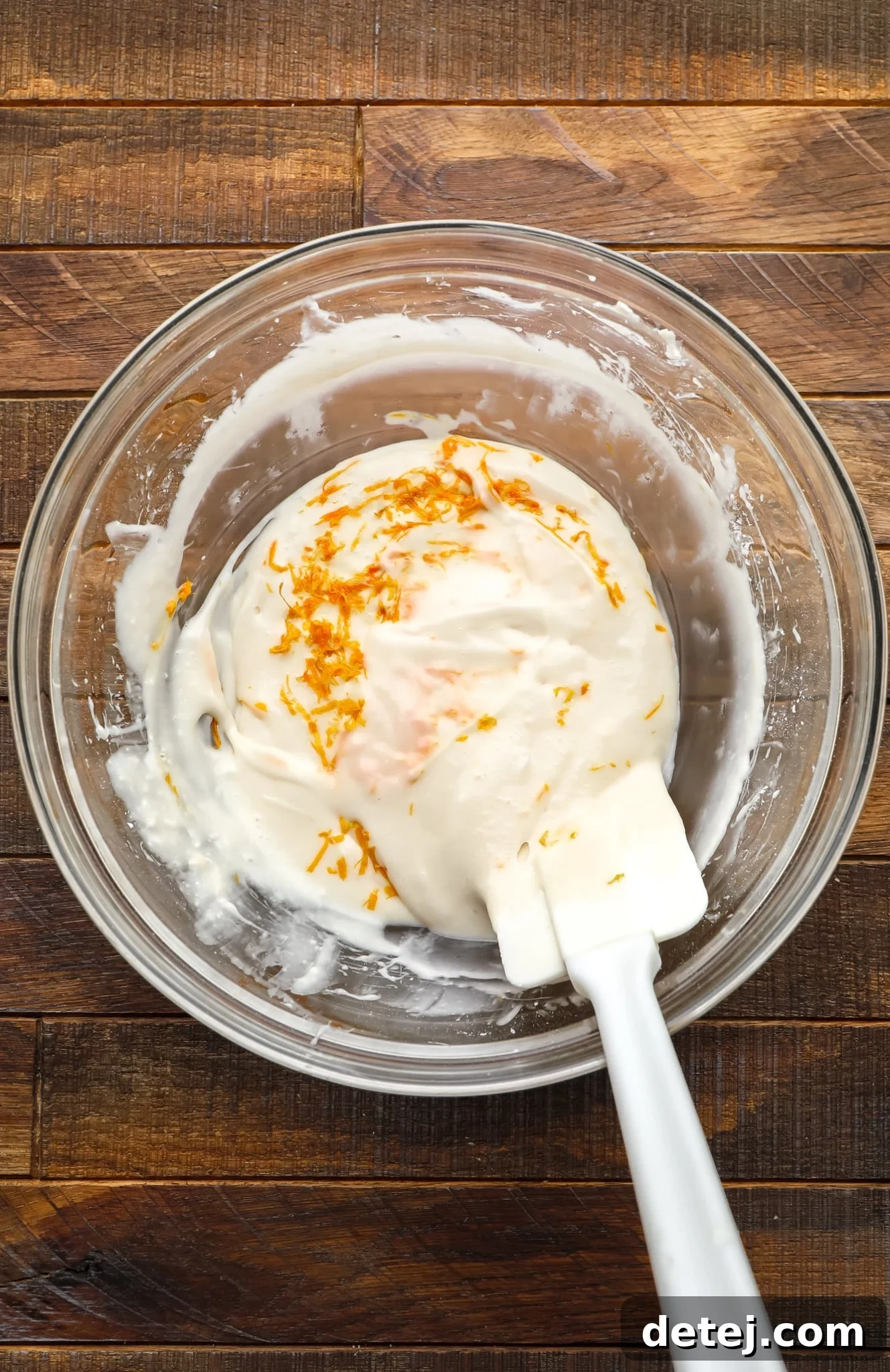 Cozy Gingerbread Bake 10 using a spatula to stir orange zest into vegan cream cheese icing.
