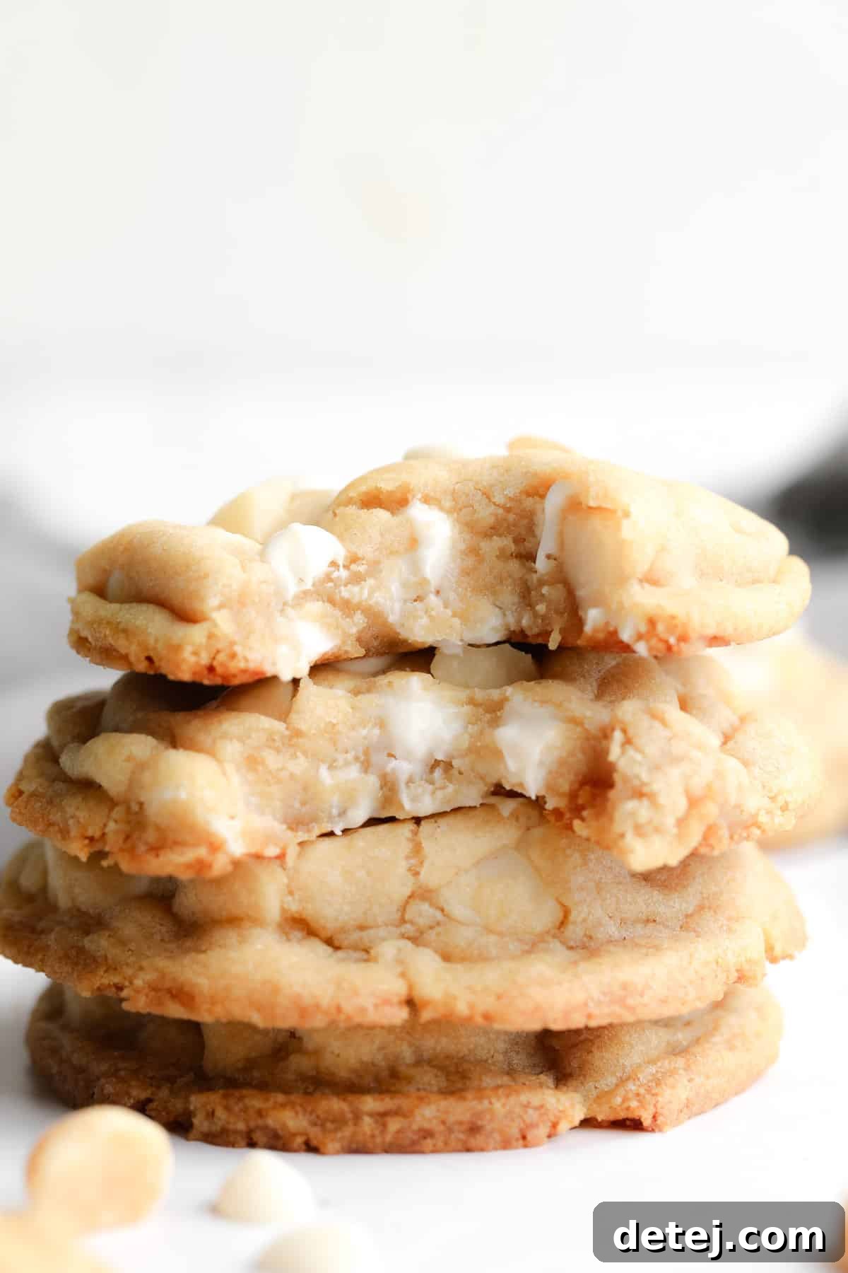 A stack of golden brown Vegan White Chocolate Macadamia Nut Cookies with bites taken out of them, showcasing their soft interior and generous chunks of white chocolate and macadamia nuts.
