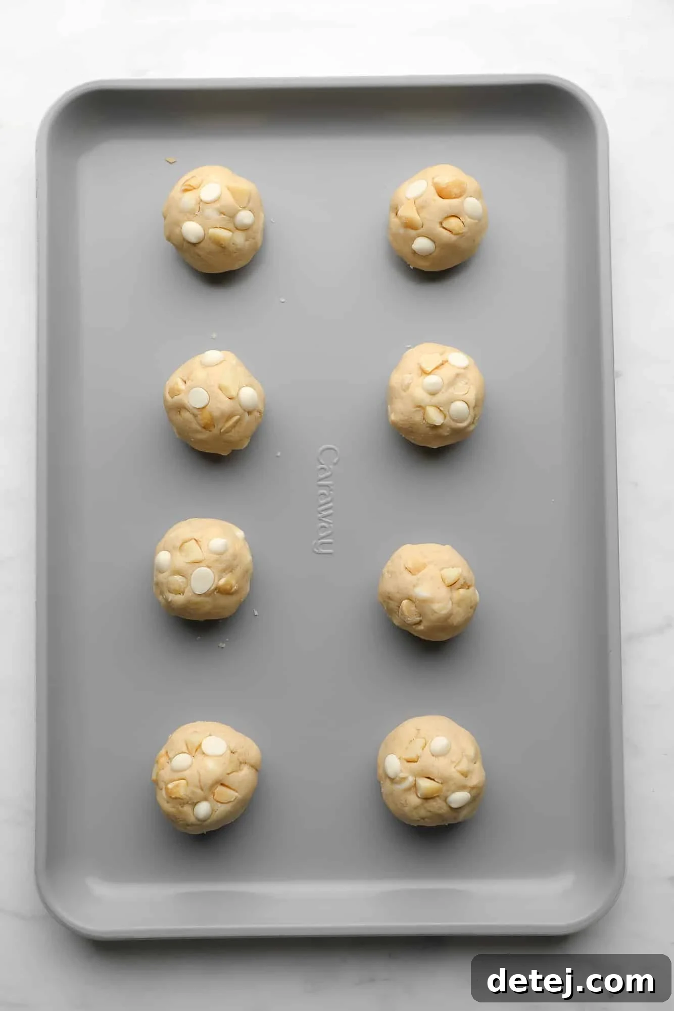Vegan White Chocolate Macadamia Nut Cookie dough balls neatly arranged on a metal baking sheet, ready for chilling and baking.