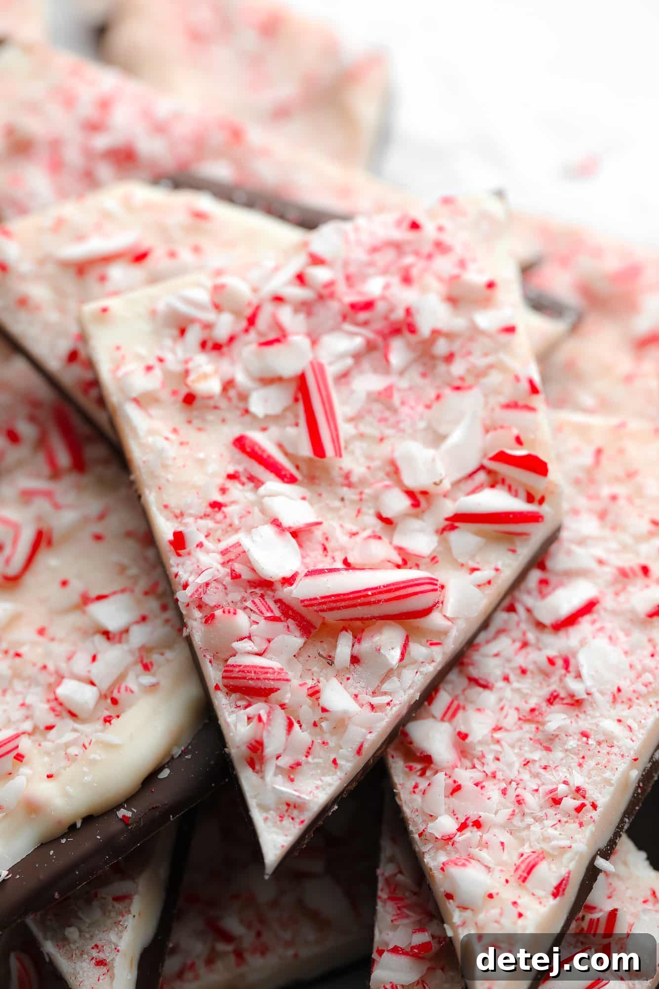 close up on a piece of vegan peppermint bark with distinct layers of dark chocolate, white chocolate, and vibrant crushed candy canes on top.