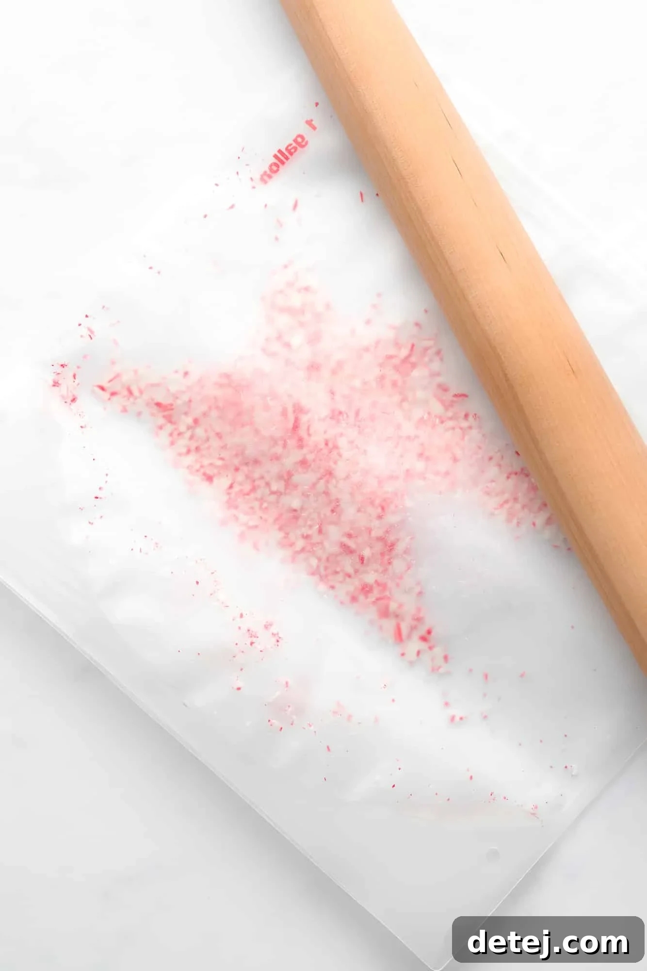Using a wooden rolling pin to expertly crush candy canes within a clear plastic bag on a wooden surface.