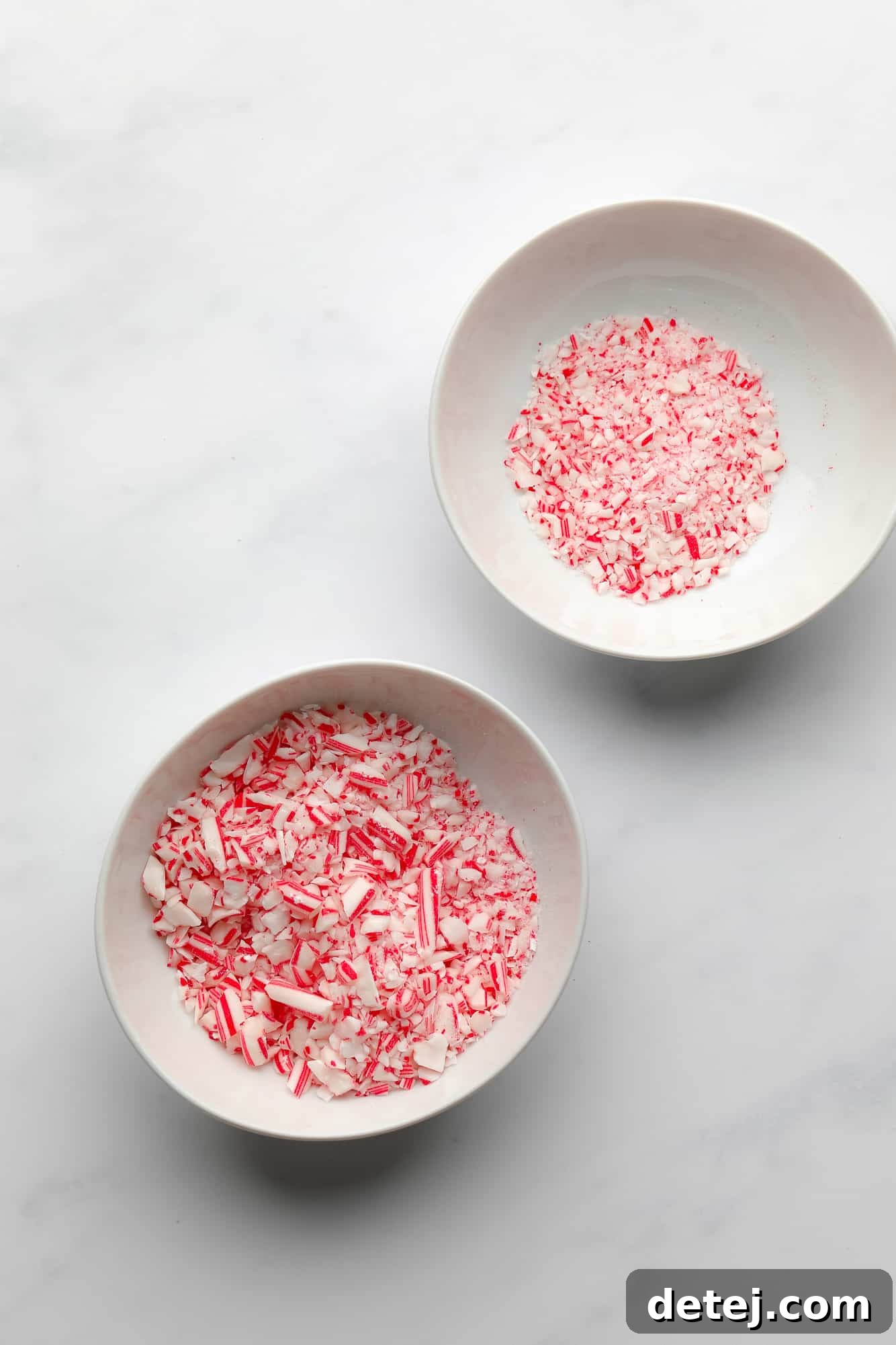 Two white bowls, one filled with finely crushed candy cane powder, and the other with larger candy cane chunks, ready for use.