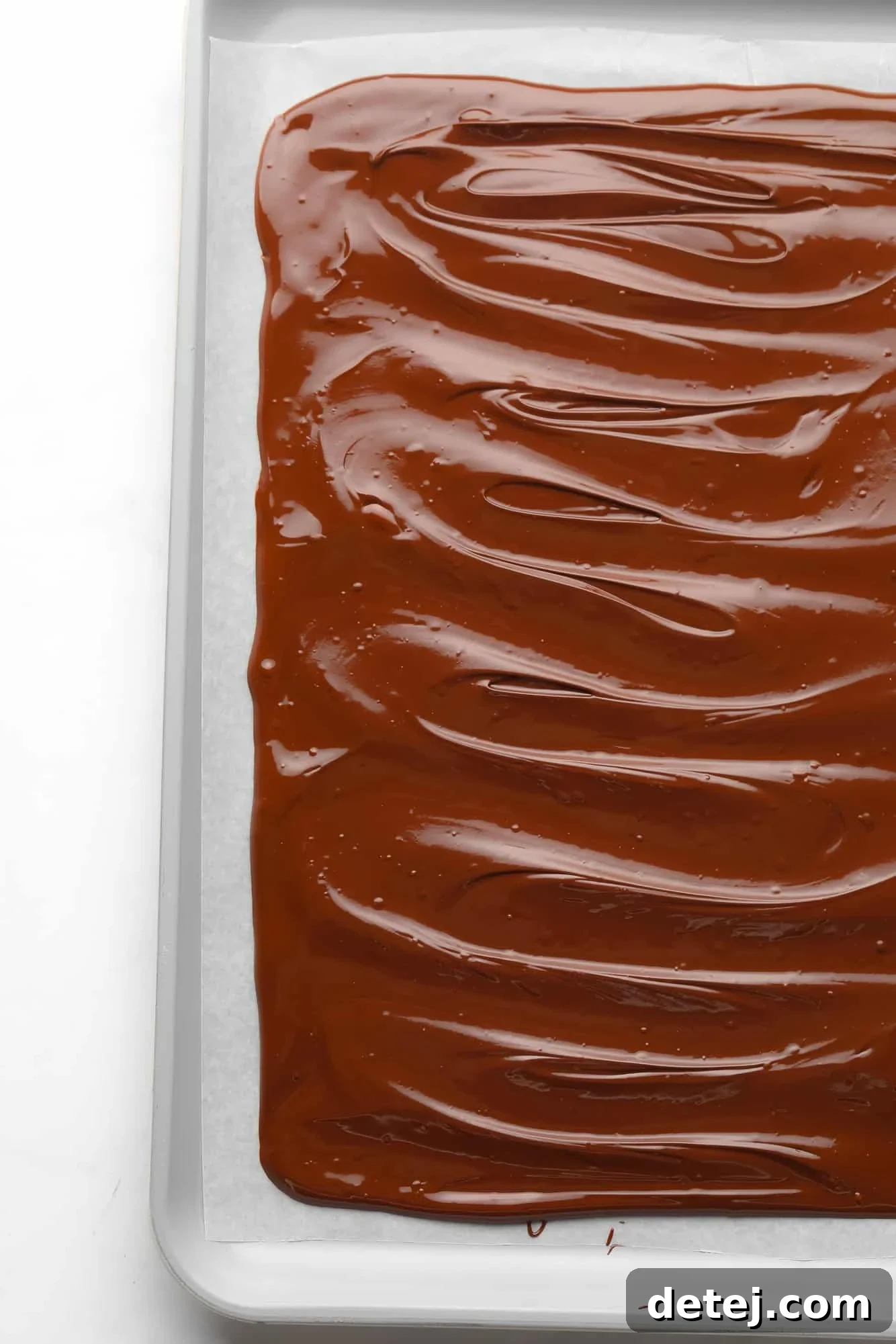 Melted dark chocolate, evenly spread into a rectangular shape on a parchment-lined baking sheet, waiting for the next layer.