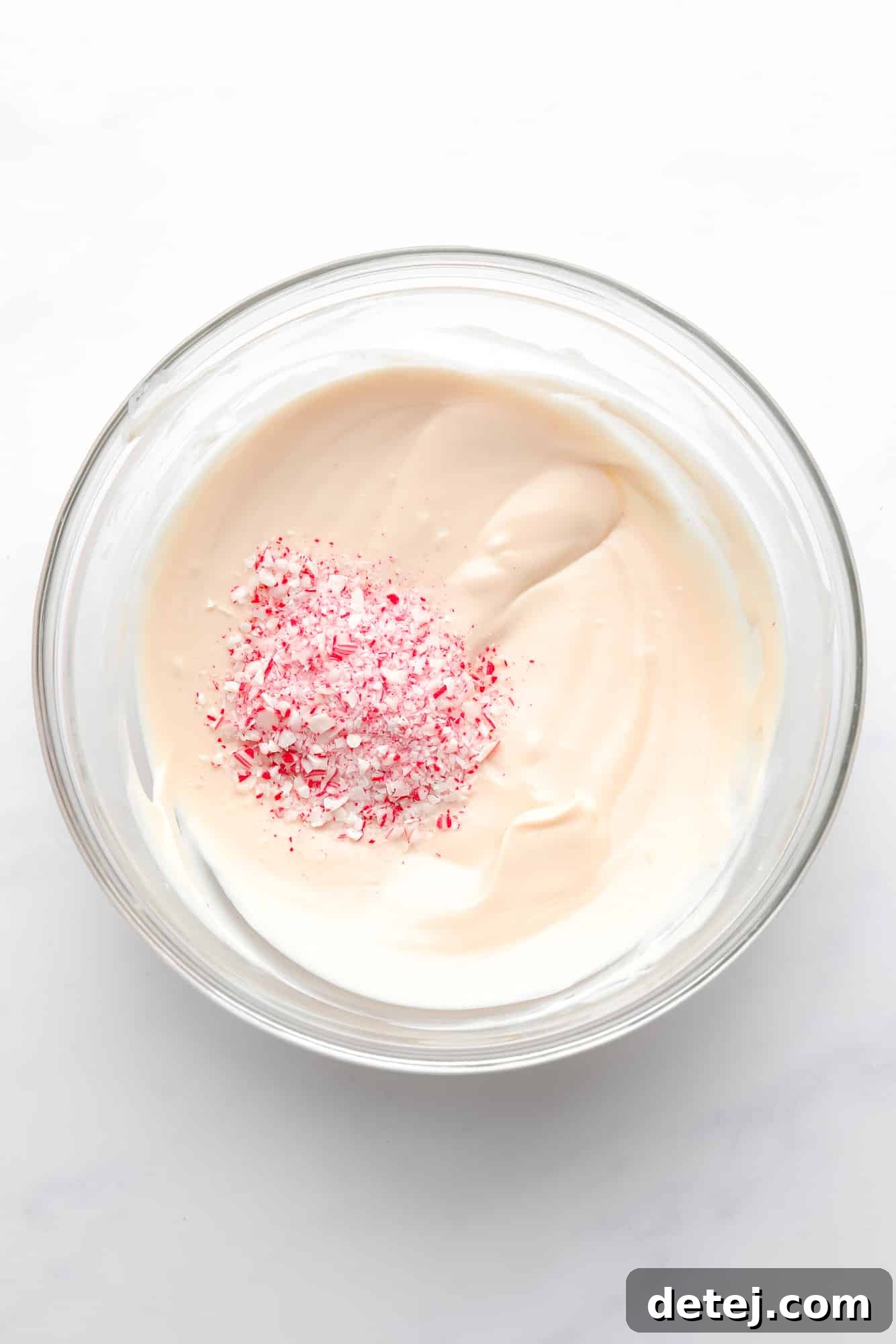 A generous pile of finely crushed candy canes being stirred into a bowl of smooth, melted vegan white chocolate.