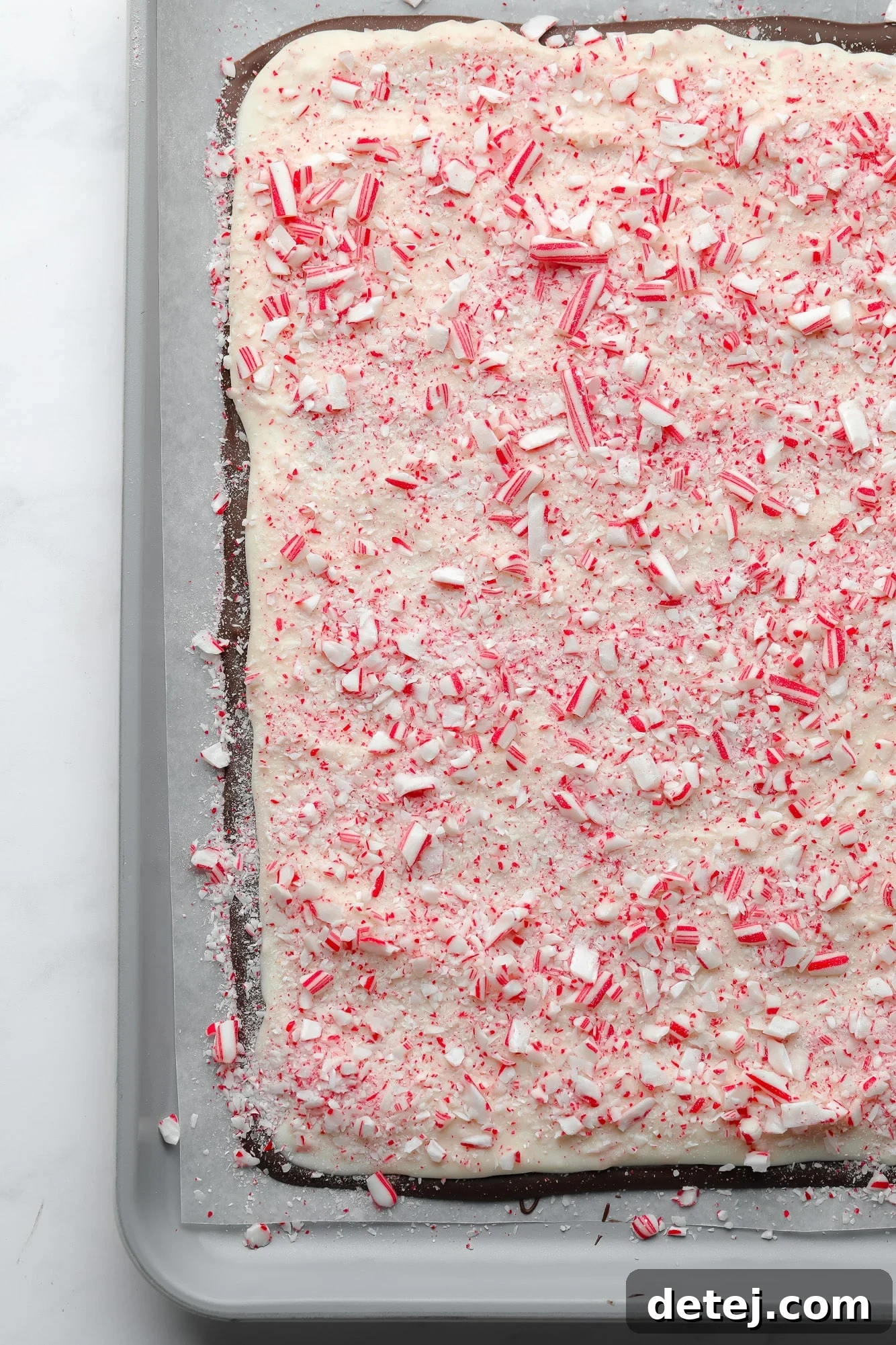 A pristine sheet of vegan peppermint bark, beautifully topped with vibrant crushed candy canes, resting on a parchment-lined baking sheet.