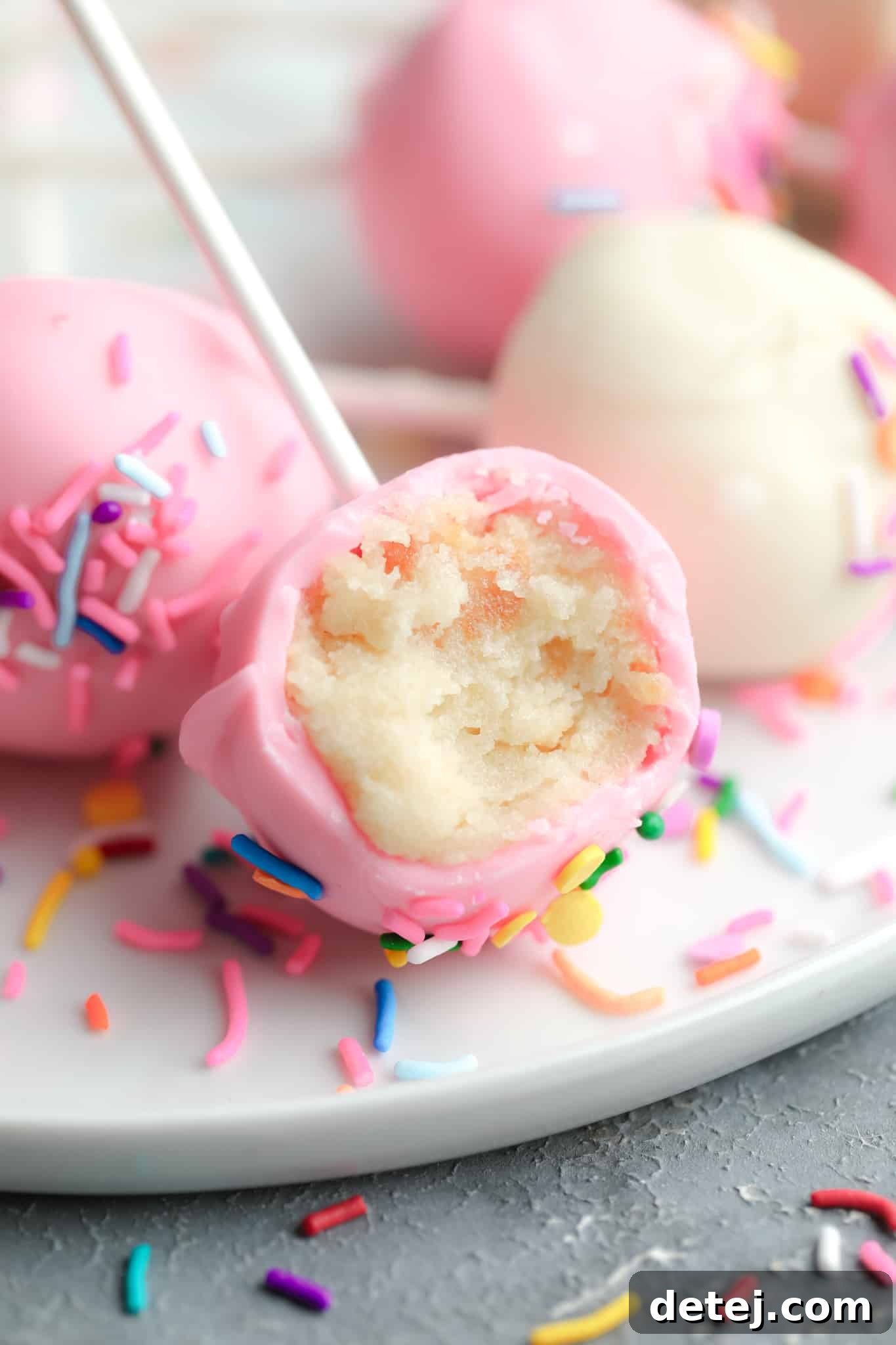 Close-up of a pink vanilla vegan cake pop with a bite taken out, showing the moist cake interior.