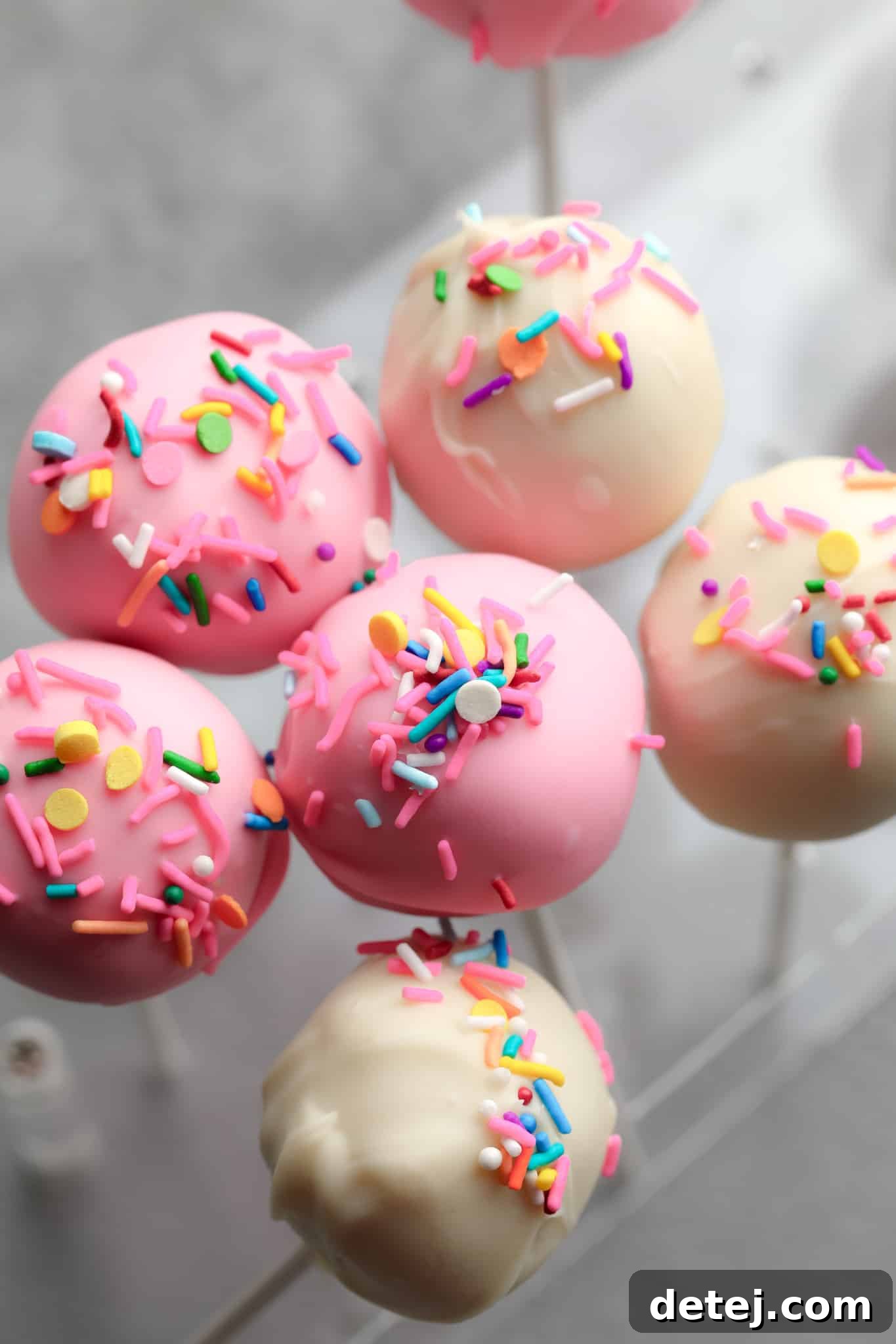 An array of pink and white vegan cake pops decorated with vibrant, colorful sprinkles.