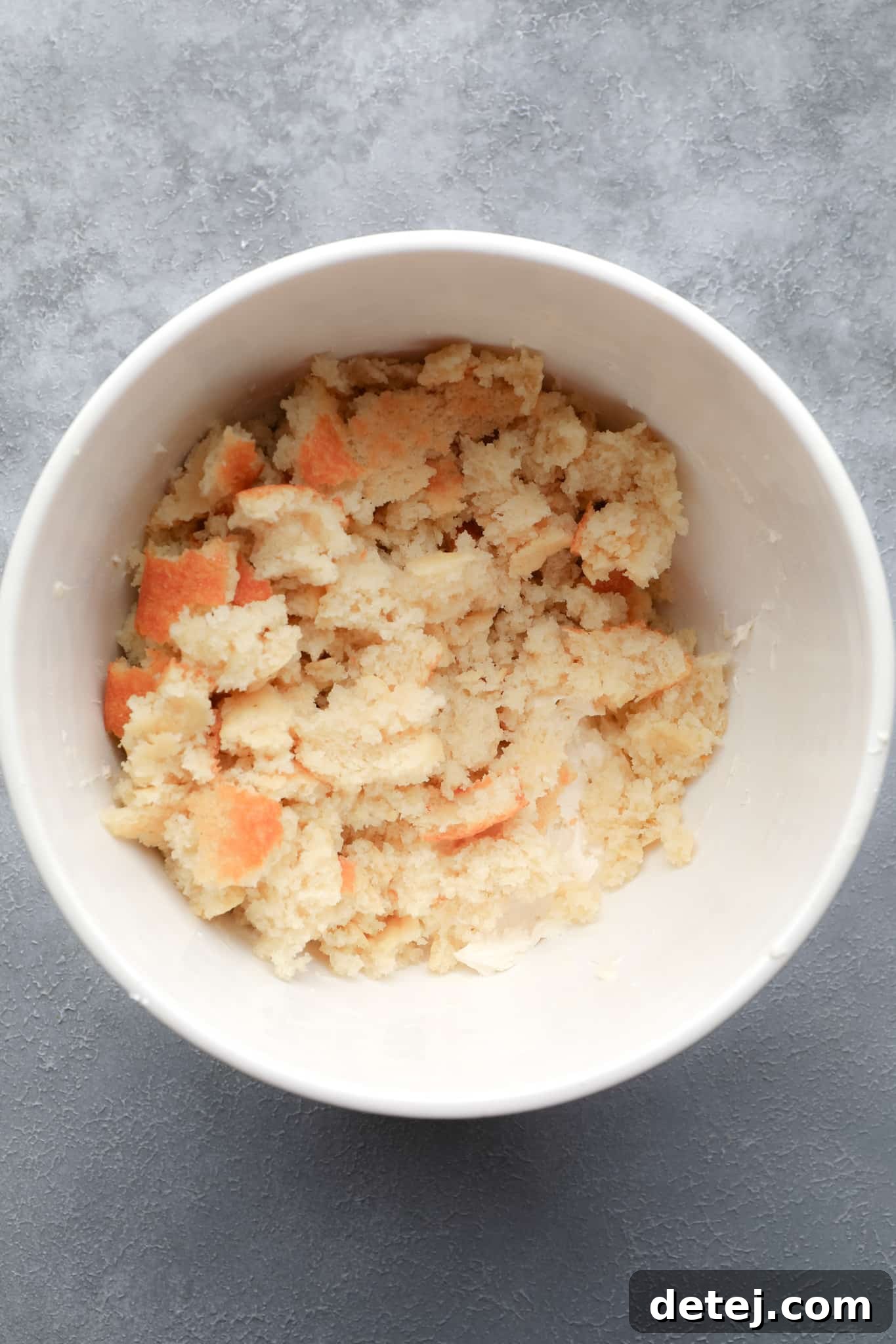 A large white bowl filled with finely crumbled vegan vanilla cake, ready for mixing with frosting.