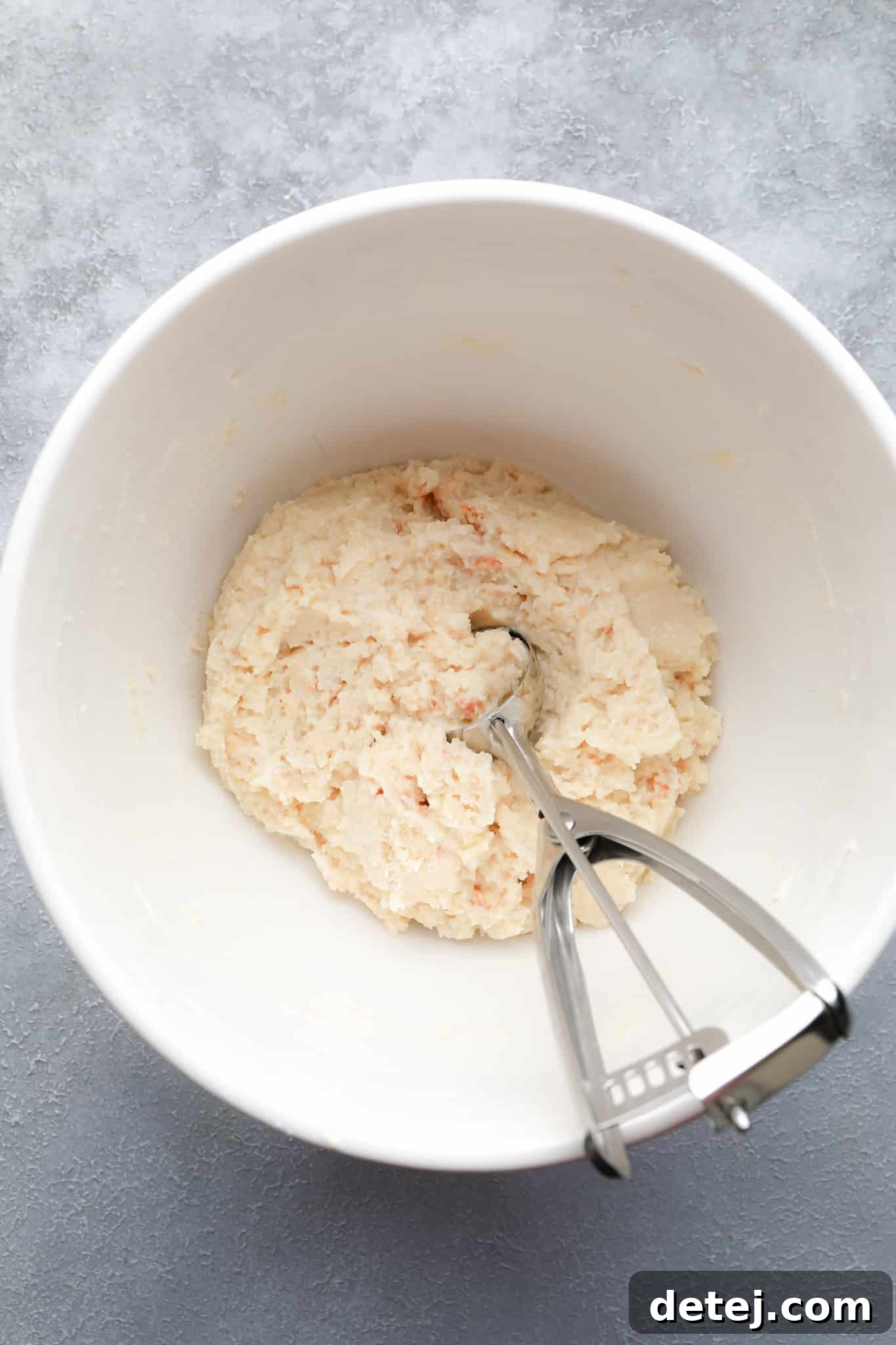 Using a cookie scoop to portion a scoop of crumbled vegan cake and frosting mixture from a white bowl.