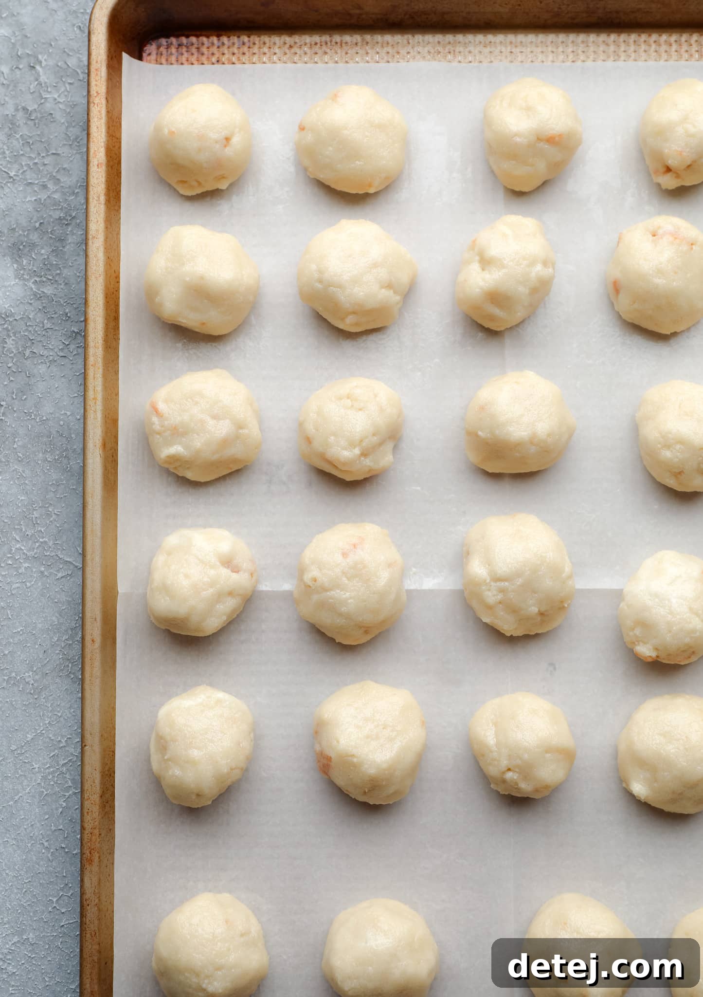 Neatly arranged rows of rolled vanilla cake balls on a parchment-lined baking sheet, chilling.