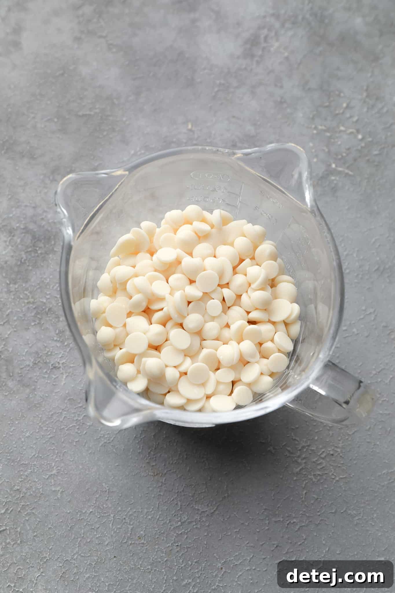 Vegan white chocolate chips ready for melting in a clear glass measuring cup.