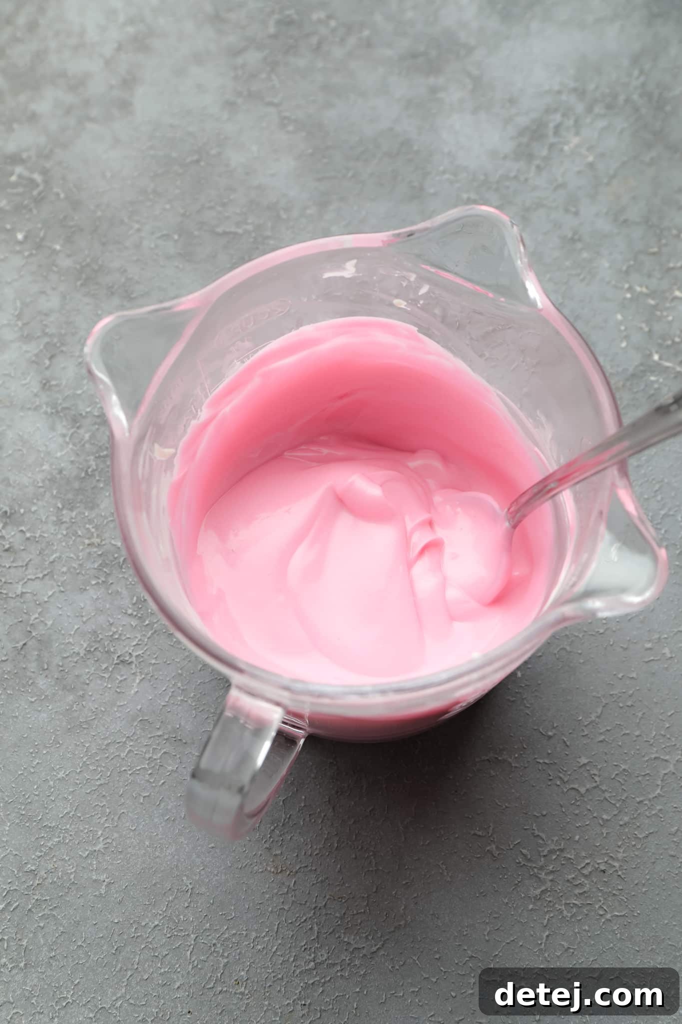 Smooth, melted pink chocolate in a glass measuring cup, ready for dipping vegan cake pops.