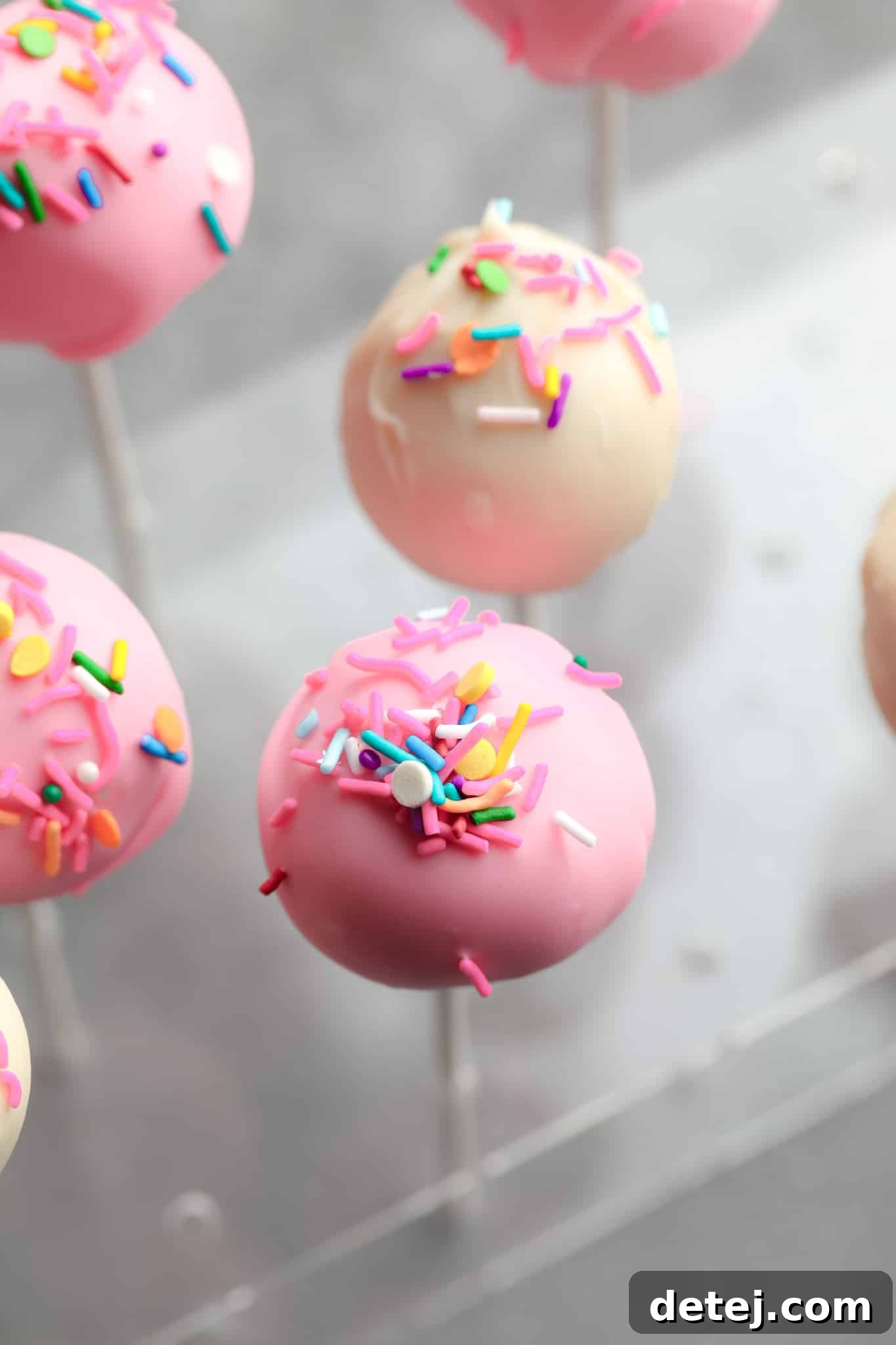 A charming display of pink and white vegan cake pops, adorned with festive colorful sprinkles.