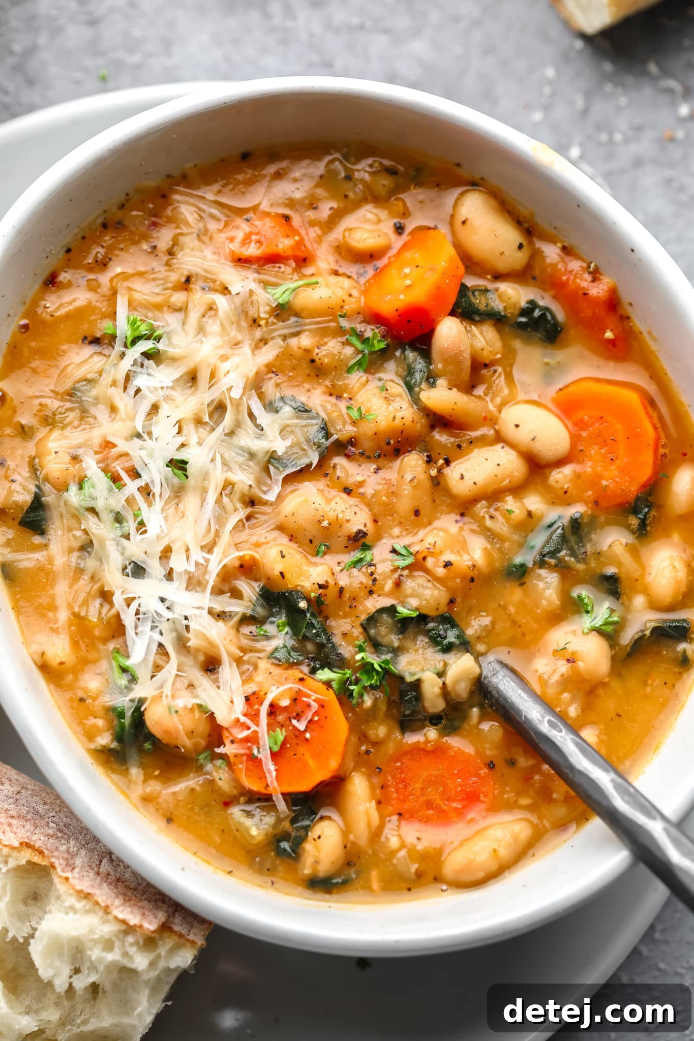 A white bowl filled with creamy white bean soup, garnished with shredded vegan parmesan cheese.