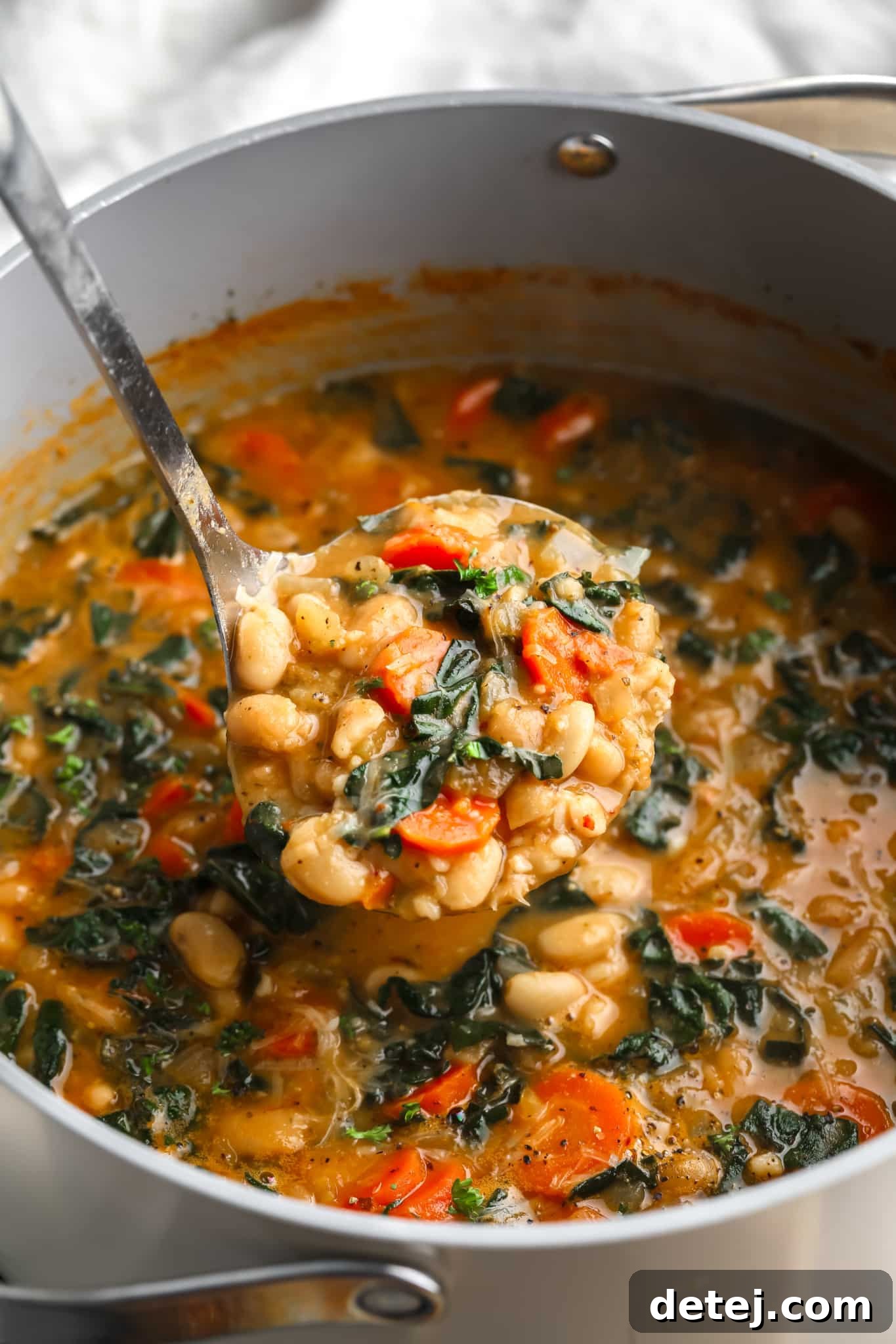 A metal ladle scooping creamy white bean soup from a large pot.