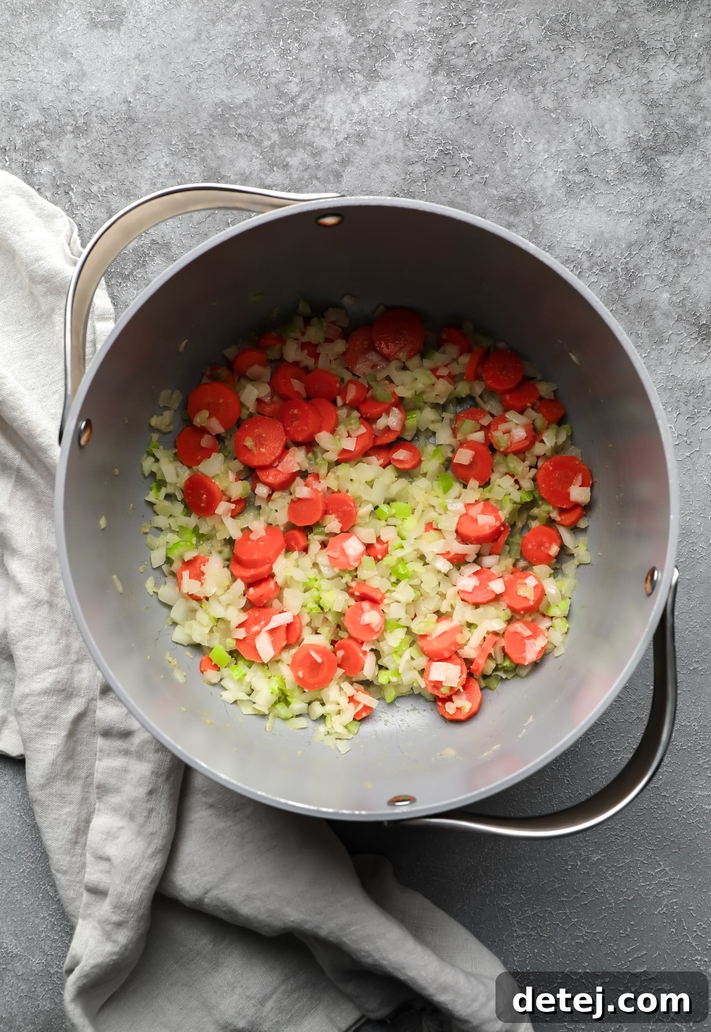 Carrots, onions, and celery cooking in a large grey pot, forming the aromatic base for the soup.