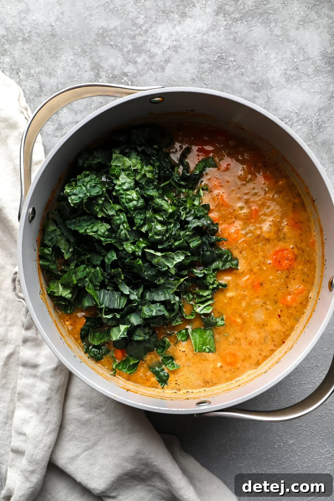 Freshly chopped kale being stirred into a large pot of simmering white bean soup.