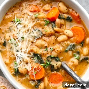A white bowl full of white bean soup topped with shredded vegan parmesan.
