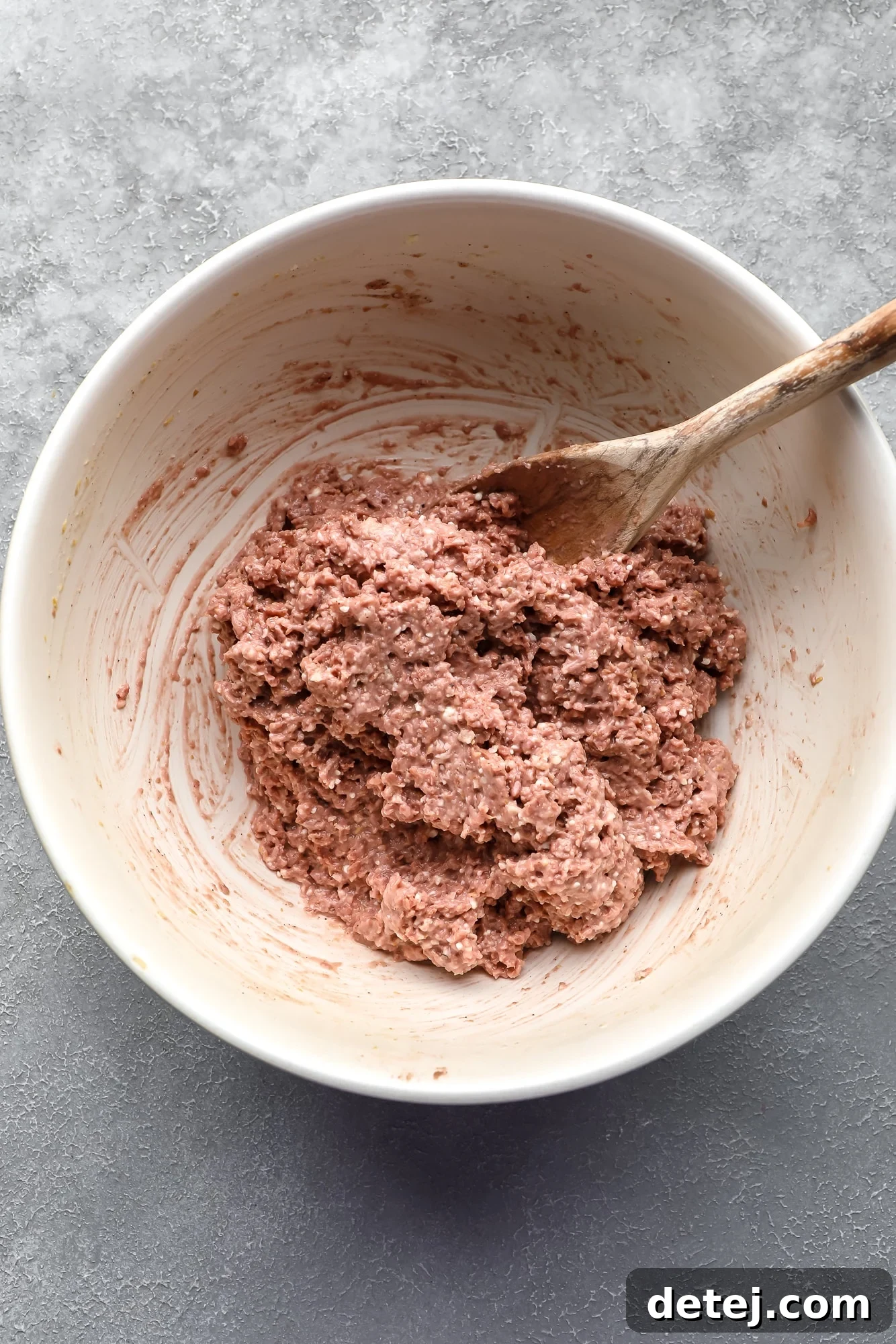 A vegan meatball mixture being diligently stirred with a wooden spoon in a spacious white bowl, showcasing the perfect consistency before rolling.