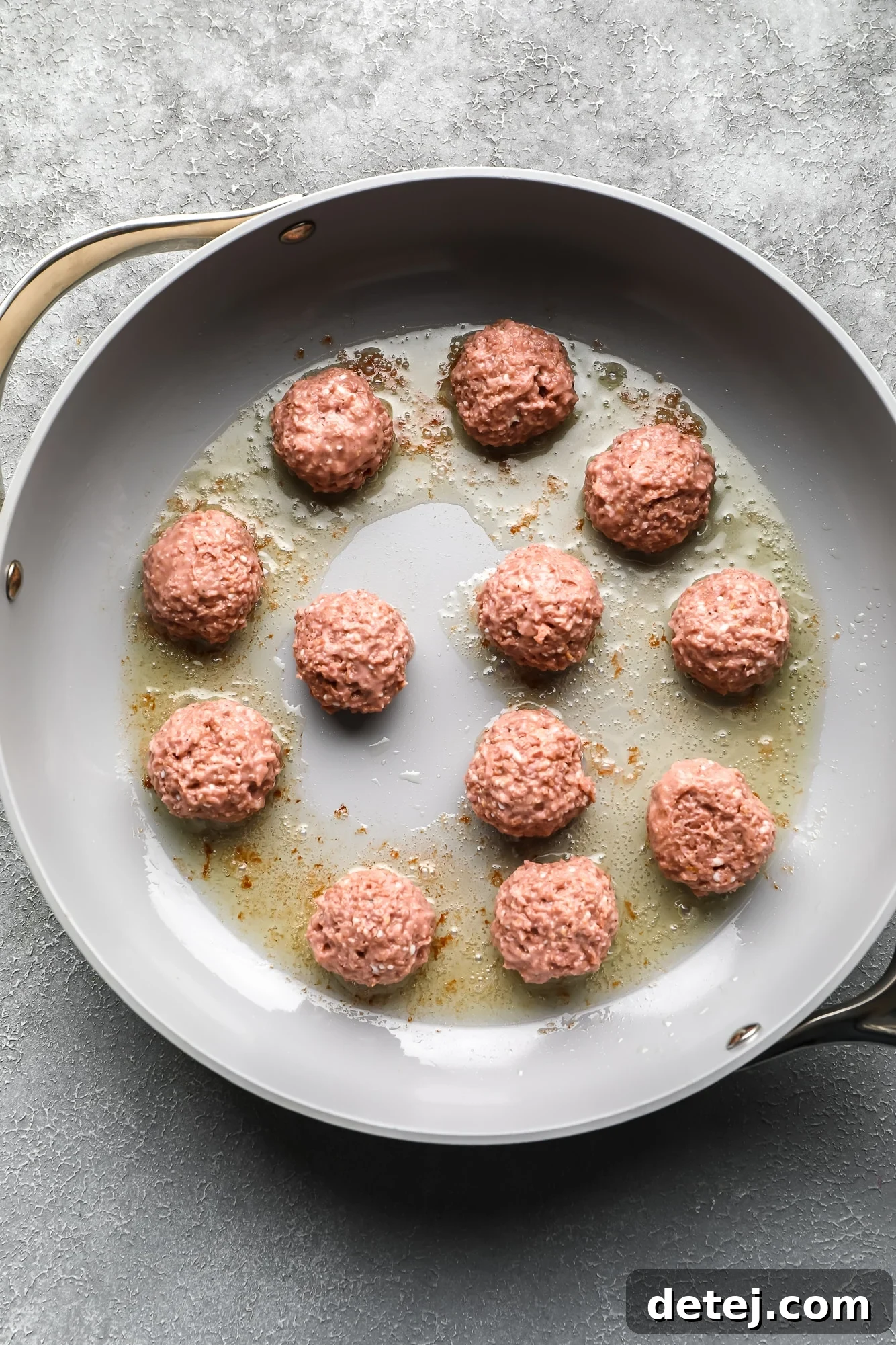 Vegan meatballs expertly frying to a perfect golden brown in a large, sturdy grey skillet, ready to be enveloped in a creamy sauce.