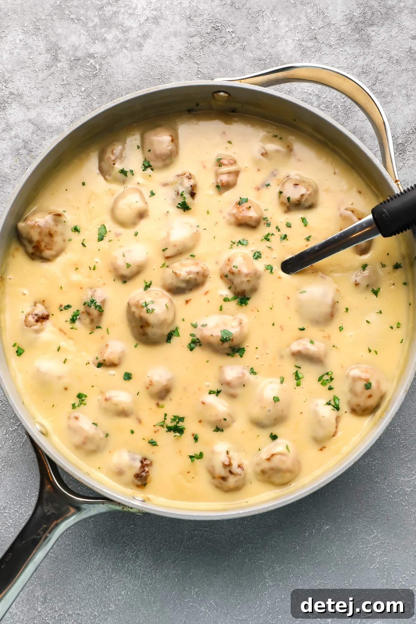 Perfectly simmered vegan Swedish meatballs bathing in a rich, creamy sauce in a large grey skillet, ready to be served.
