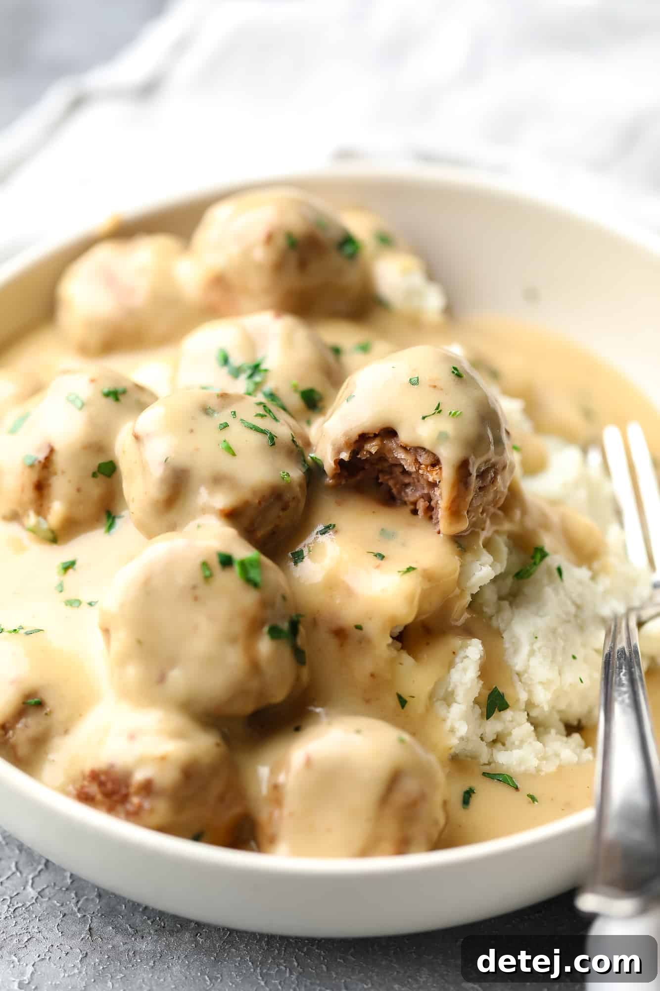 Vegan Swedish meatballs covered in a creamy gravy and served on top of mashed potatoes in a white bowl with a fork.