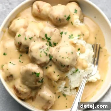 vegan Swedish meatballs covered in a creamy gravy and served on top of mashed potatoes in a white bowl with a fork.