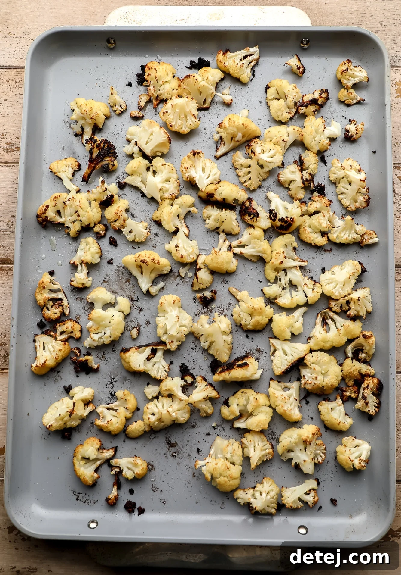 Perfectly roasted cauliflower florets, golden and slightly charred, spread evenly on a large metal baking sheet.