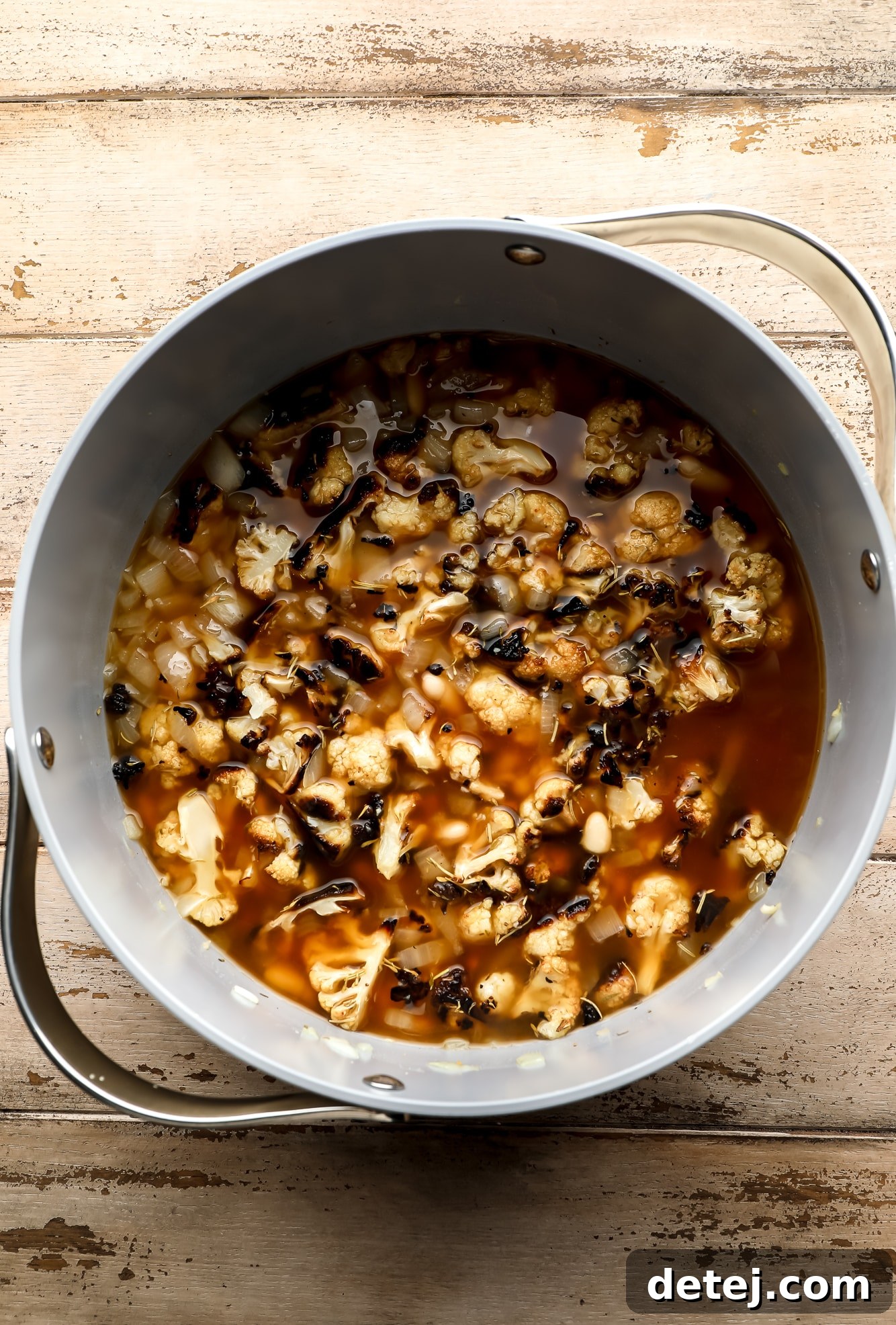 A large grey pot filled with the ingredients for roasted cauliflower soup before blending: sautéed onions, garlic, cannellini beans, herbs, broth, and roasted cauliflower florets.