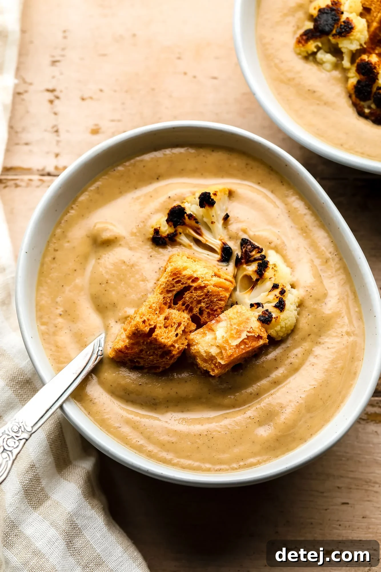 A beautifully presented bowl of creamy roasted cauliflower soup, adorned with golden croutons and perfectly charred cauliflower florets, ready to be enjoyed.